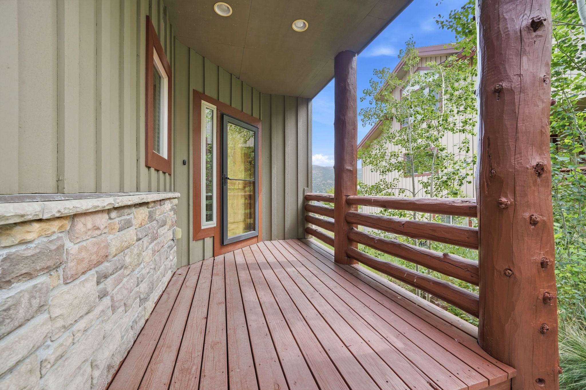 Covered porch featuring wood-finish decking, natural log railings, and a stone veneer half-wall