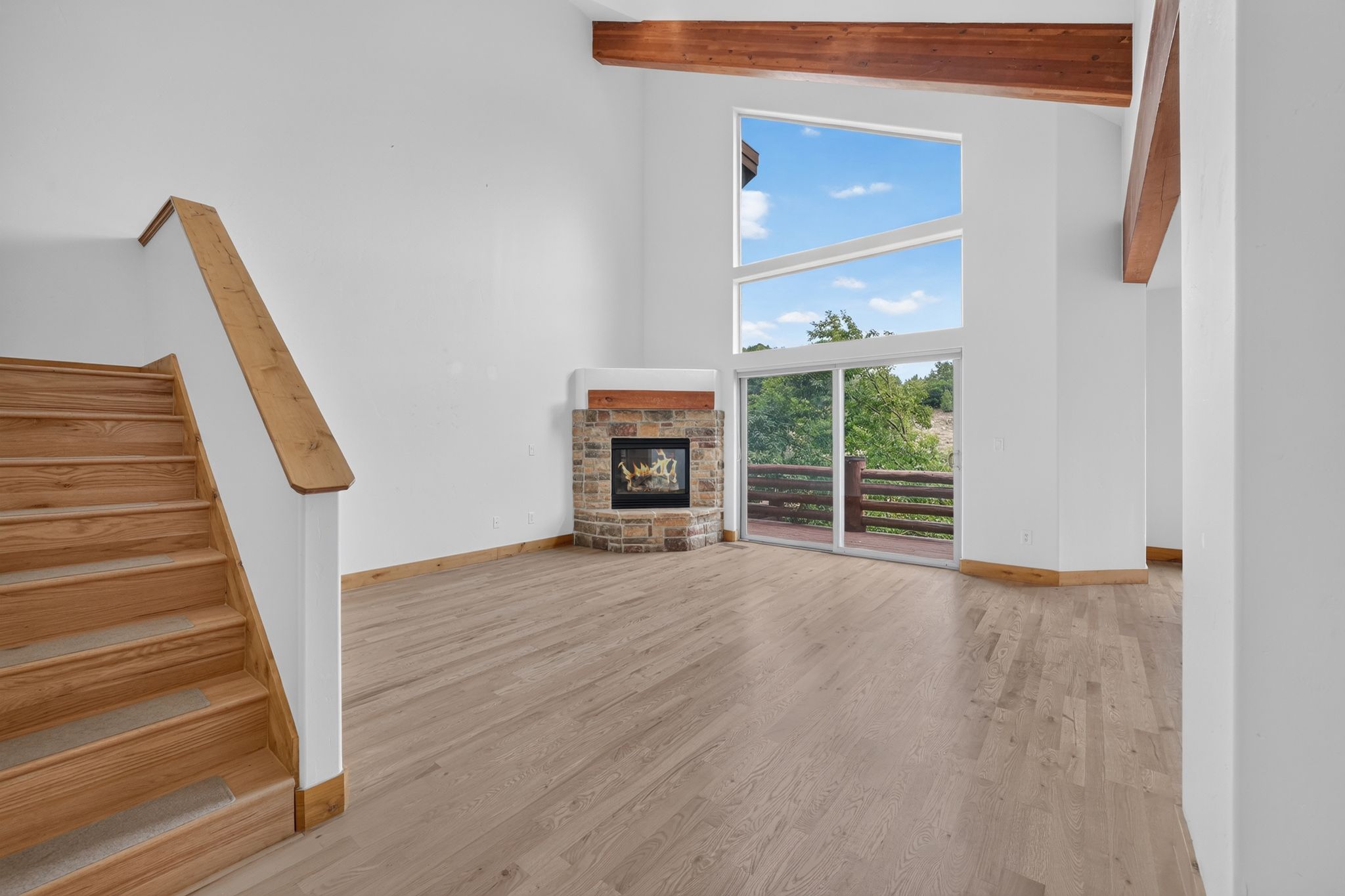 Spacious living area featuring a stone-clad corner fireplace, vaulted ceiling with exposed wood beams, and a wood-finish staircase