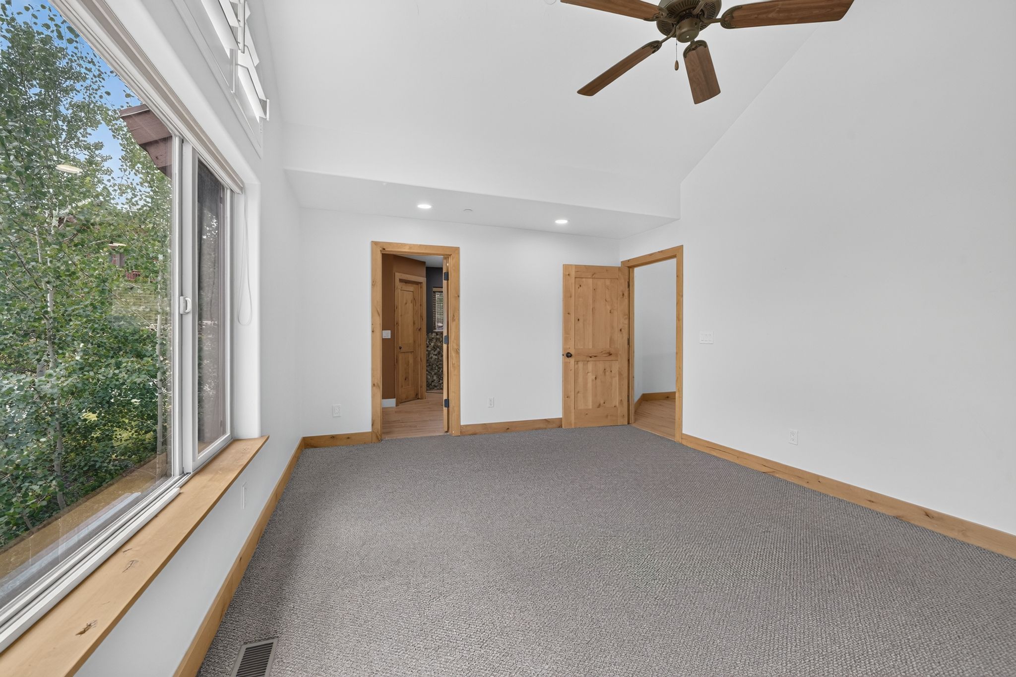 Spacious room featuring vaulted ceilings, a large window, a ceiling fan, and carpeted flooring
