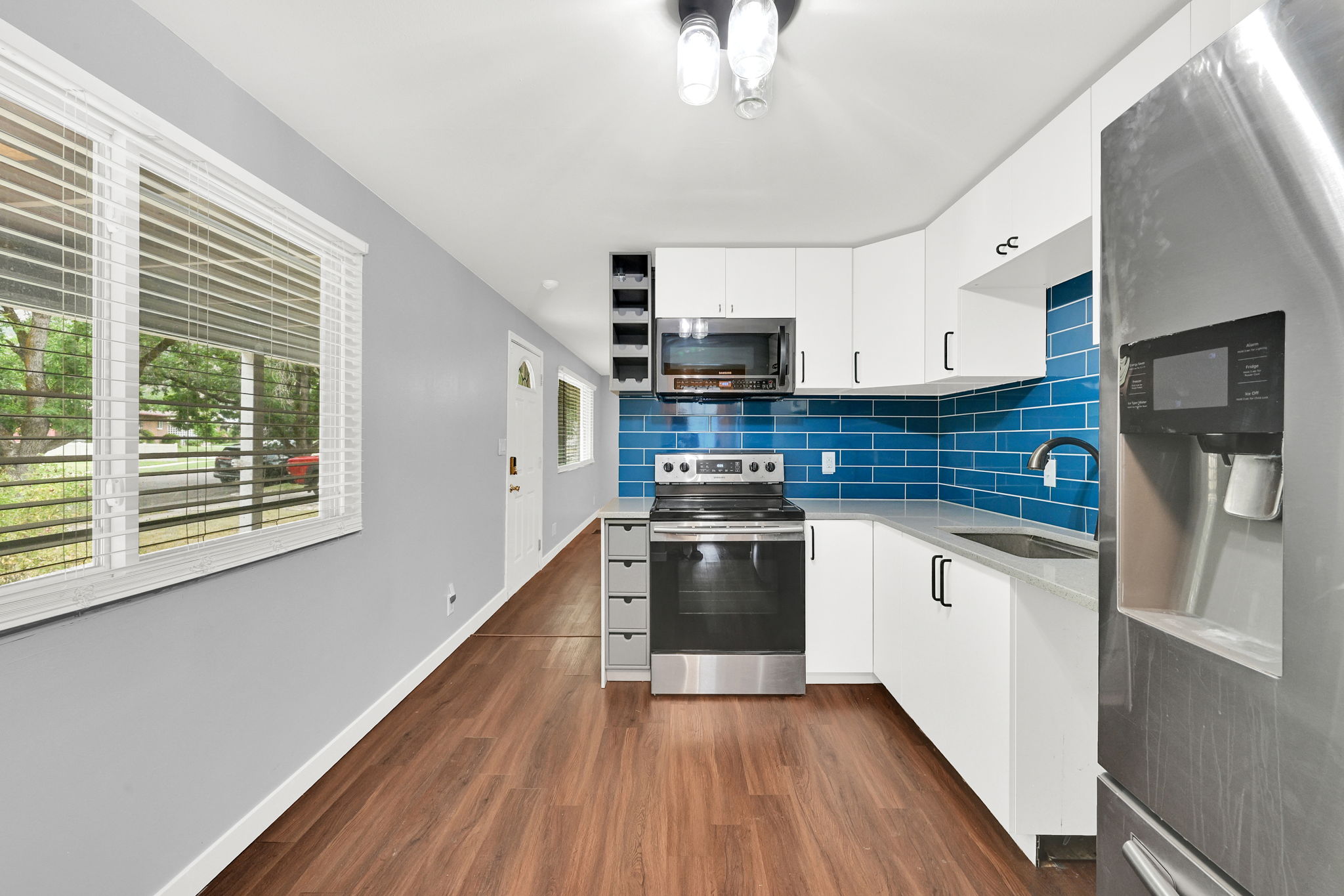 Modern kitchen featuring white cabinetry, a blue subway tile backsplash, stainless steel appliances, and wood-finish flooring