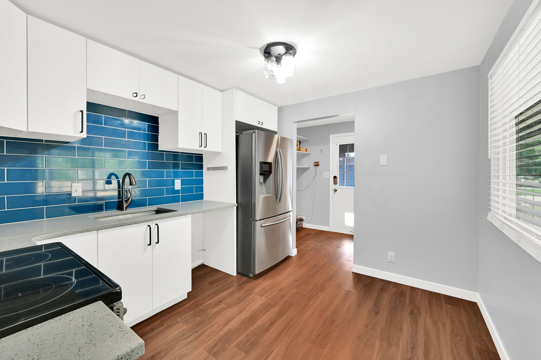 Kitchen featuring white cabinetry, blue subway tile backsplash, stainless steel appliances, wood-finish flooring, and light gray walls