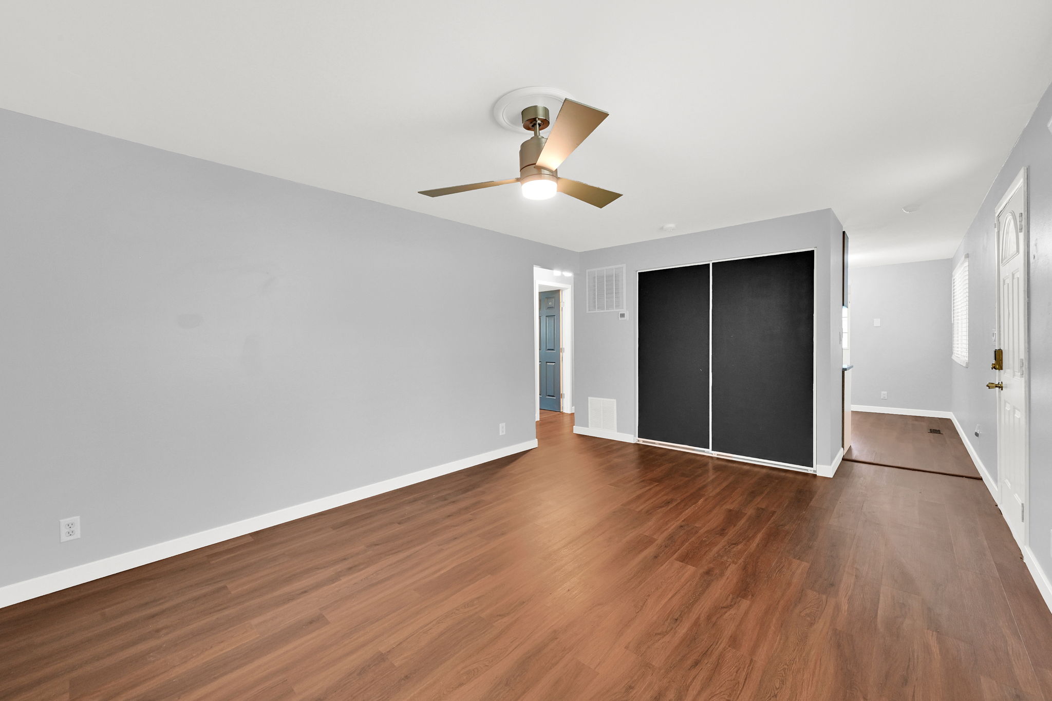 Spacious interior featuring wood-finish flooring, a contemporary ceiling fan, and light gray wall tones