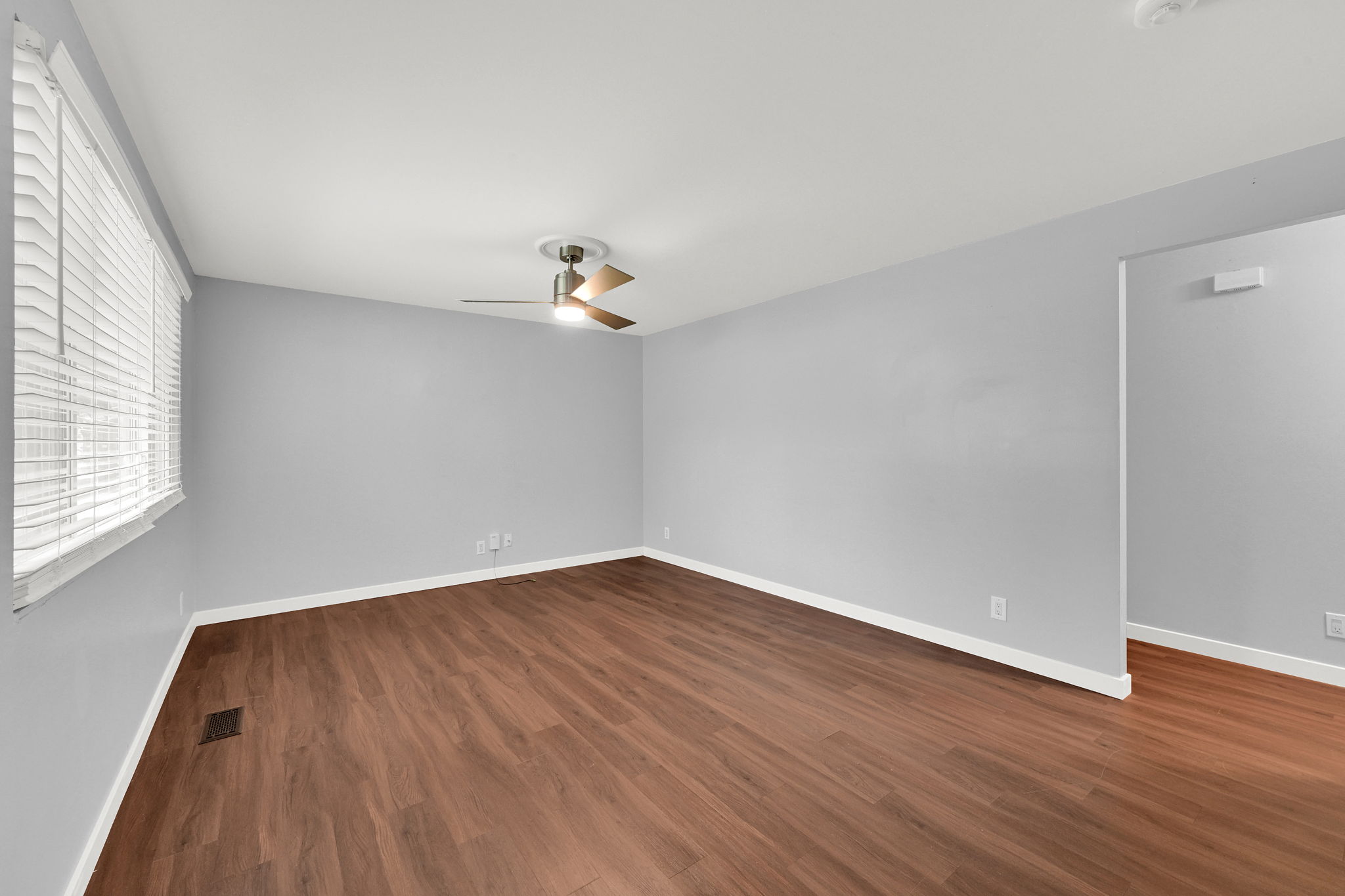 Spacious room featuring wood-finish flooring, light gray walls, white baseboards, and a ceiling fan with integrated lighting