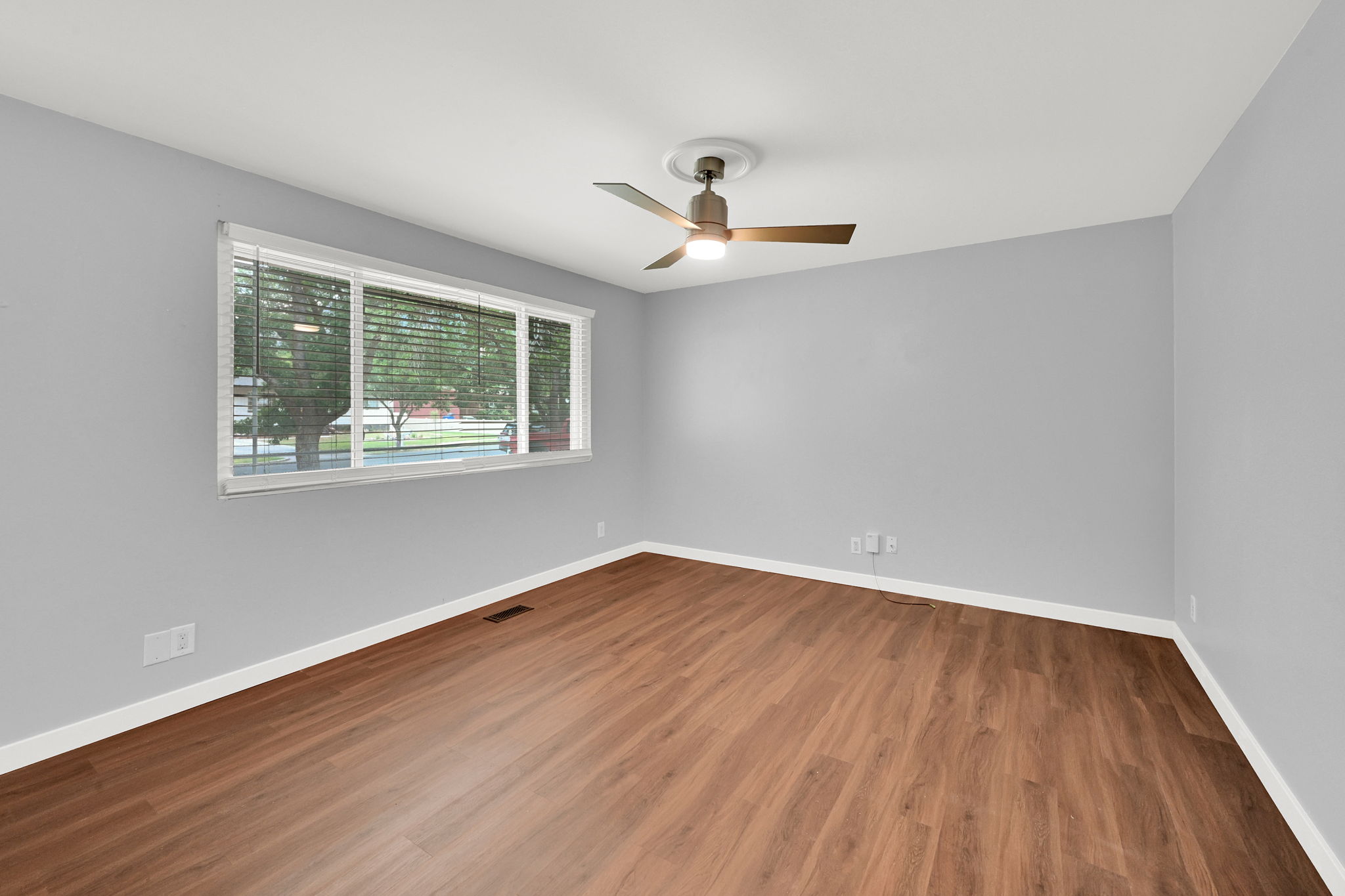 Spacious room featuring wood-finish flooring, light grey walls, white baseboards, and a modern ceiling fan