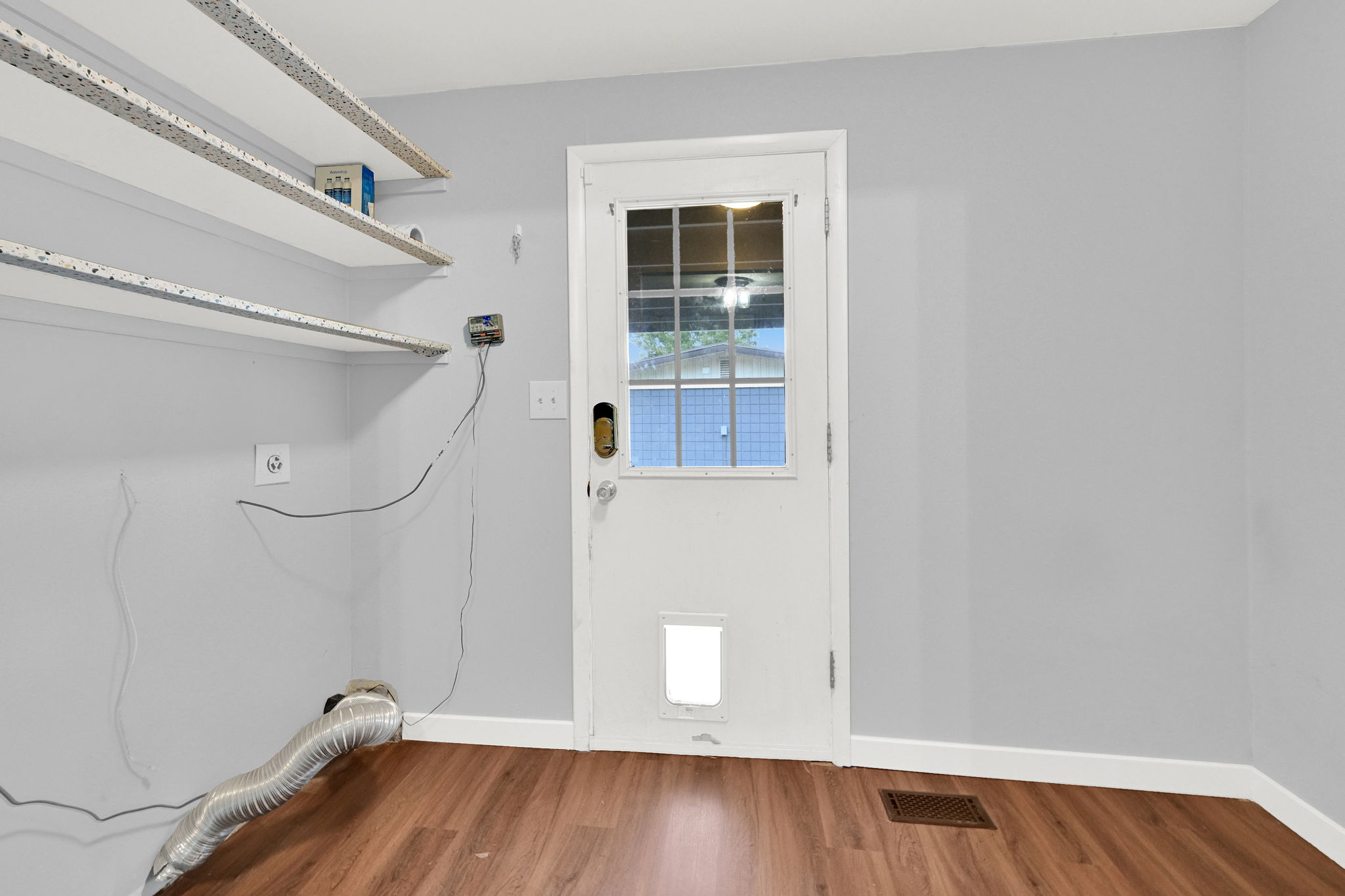 Utility room featuring wood-finish flooring, light gray walls, built-in shelving, and a white exterior door with a window pane