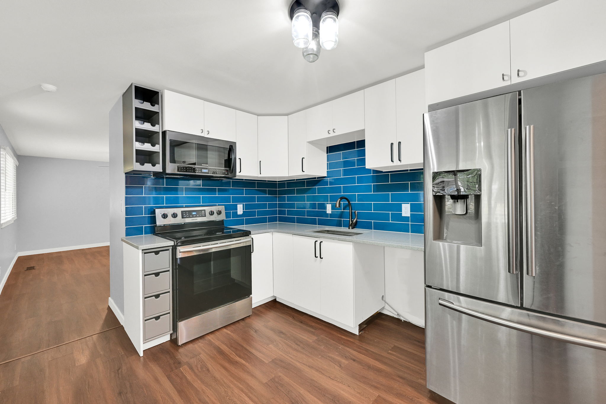 Modern kitchen featuring white cabinetry, stainless steel appliances, a vibrant blue tile backsplash, and wood-finish flooring
