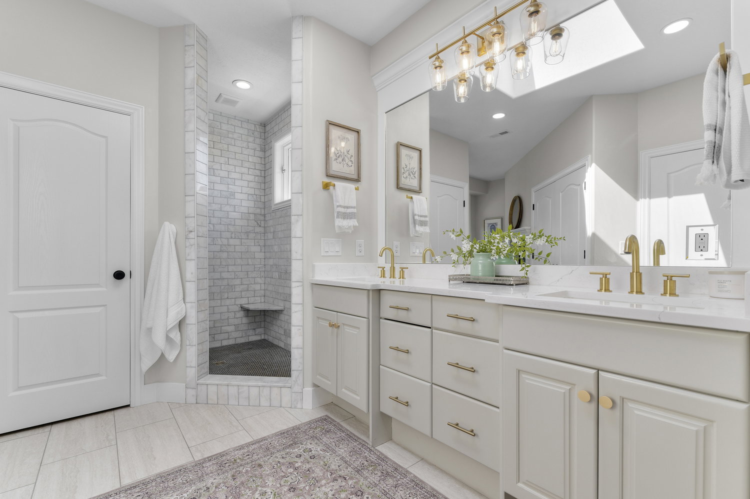 Double vanity with light-colored cabinetry, gold-toned hardware, quartz-finish countertops, and dual undermount sinks