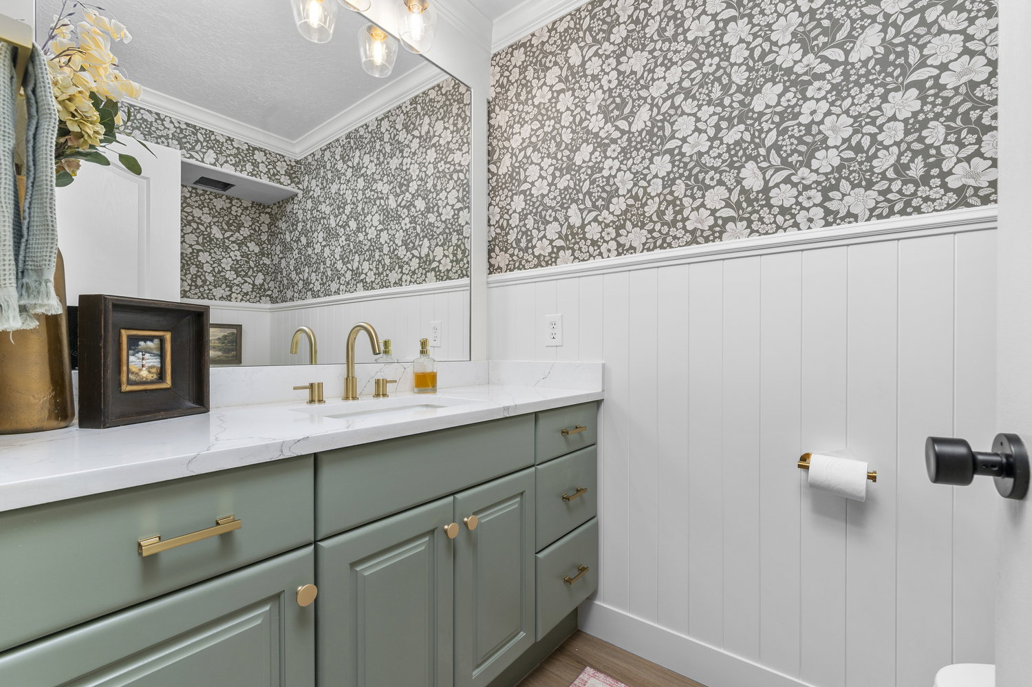 Bathroom vanity featuring a light green cabinet with gold-toned hardware, a white countertop, and an integrated rectangular sink with a gold-toned faucet