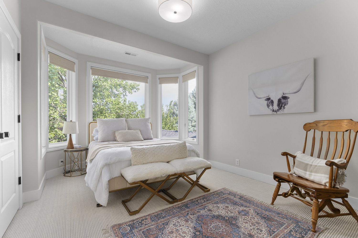Bay window with multiple large window panes, neutral roller shades, light neutral wall paint, ceiling-mounted light fixture, and textured neutral carpeting