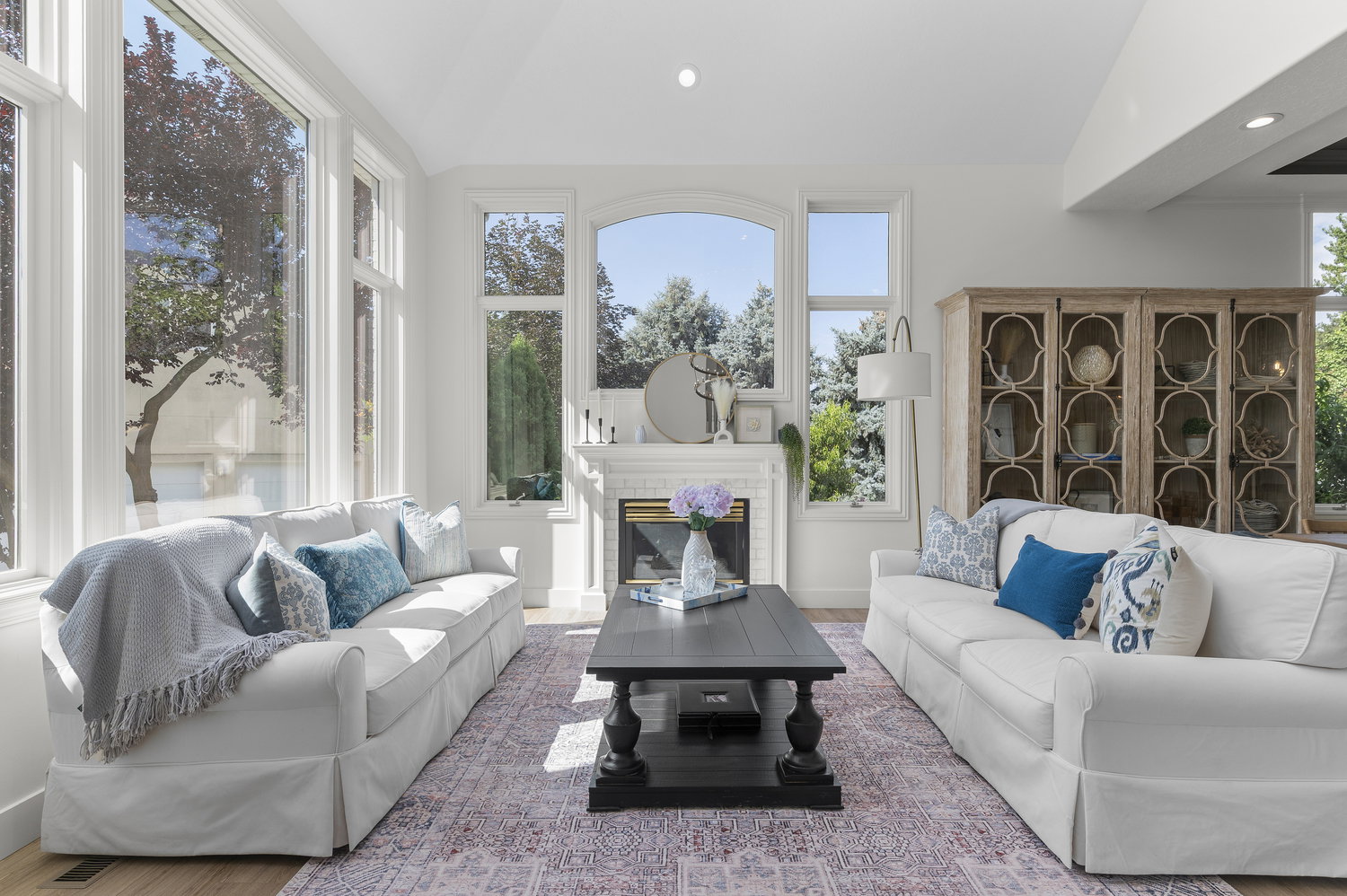 Spacious living area featuring extensive windows, a white brick fireplace, wood-finish flooring, recessed lighting, and a built-in display cabinet