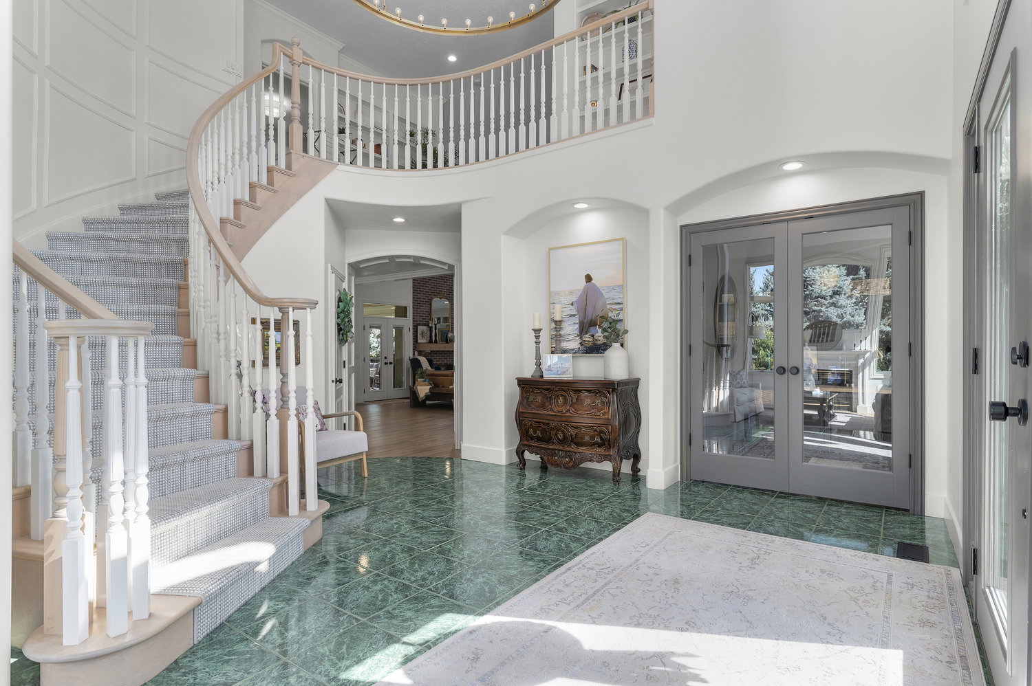 Grand foyer featuring a curved staircase with carpeted treads and wood handrails, green-hued tile flooring, a two-story ceiling, and arched doorways
