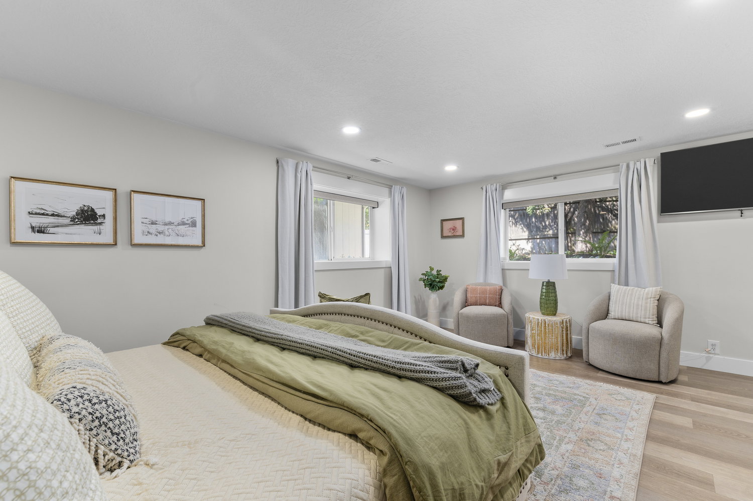 Recessed lighting illuminates this room featuring light wood-finish flooring and multiple windows with drapery