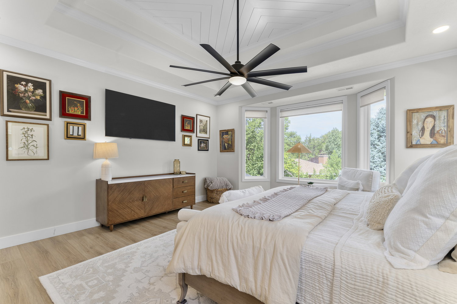 Bay window with multiple panels, wood-finish flooring, tray ceiling with geometric detailing, large ceiling fan, and white baseboards