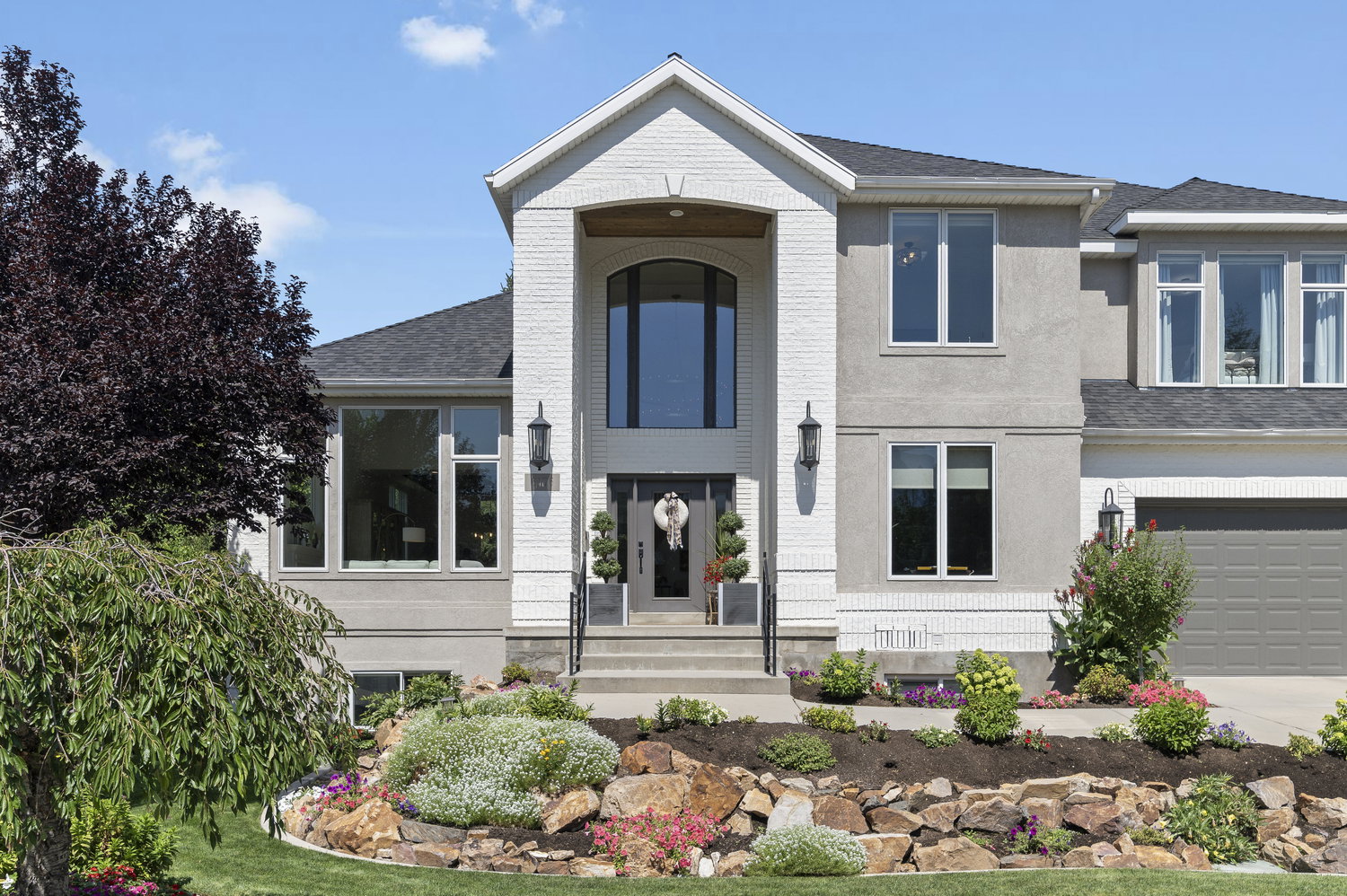 Stately two-story residence featuring a white brick and stucco exterior, arched portico entry, dark shingle roof, and a prominent arched window above the main entrance