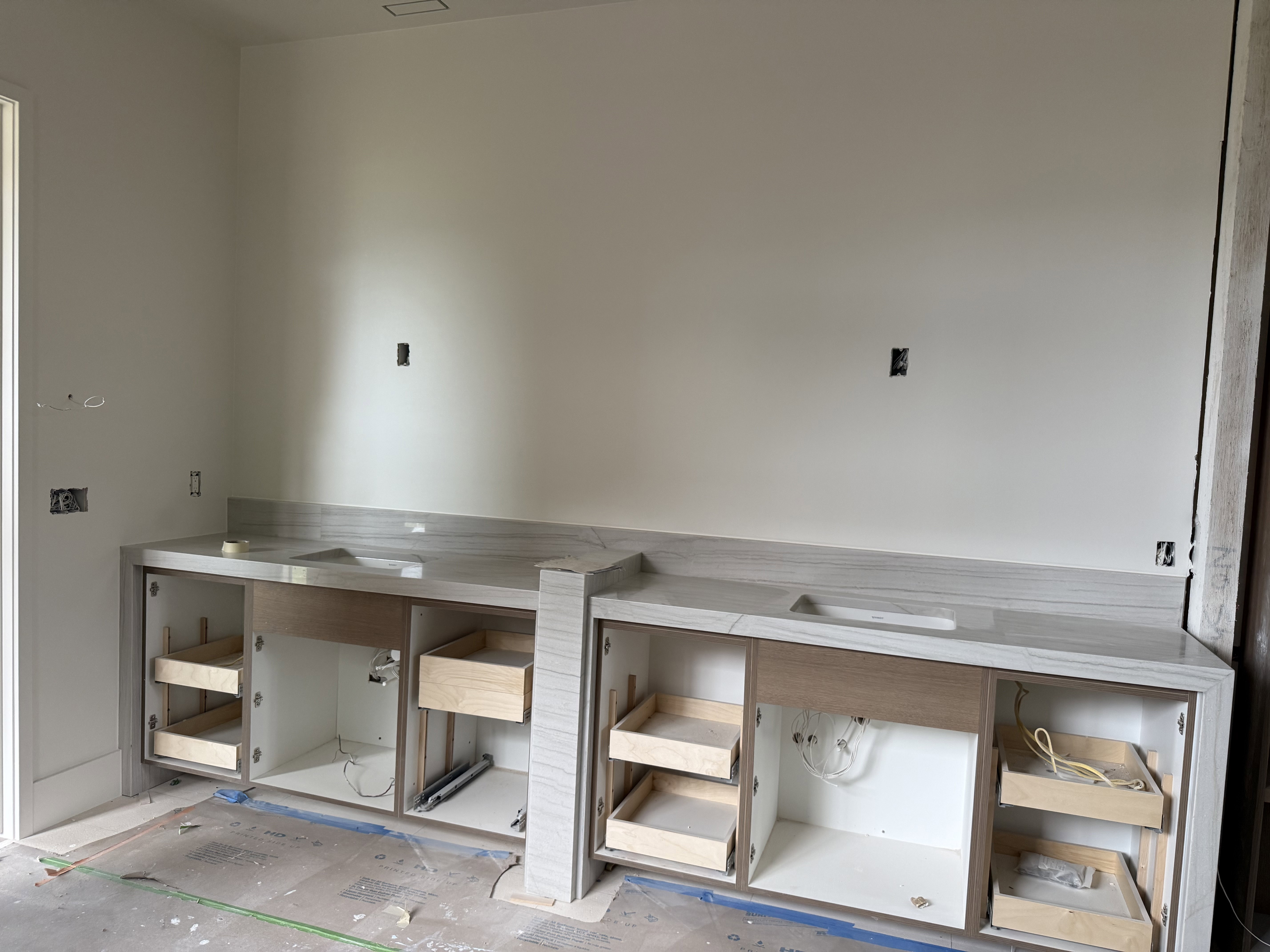 Dual vanity bases with light wood-finish cabinetry, integrated sinks, and matching stone countertops with backsplash
