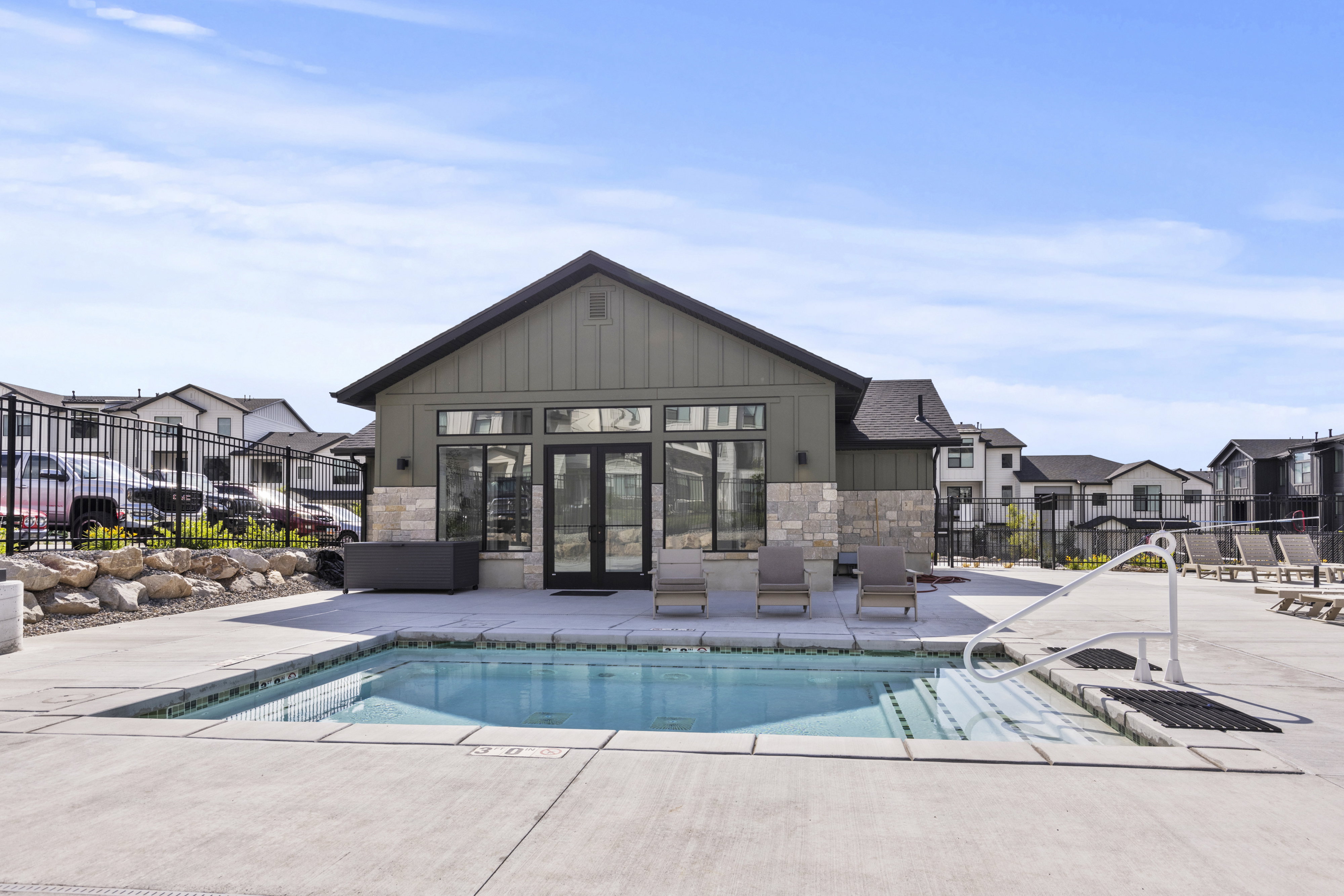 Modern pool area featuring a concrete deck, built-in hot tub, and a contemporary clubhouse with board and batten siding