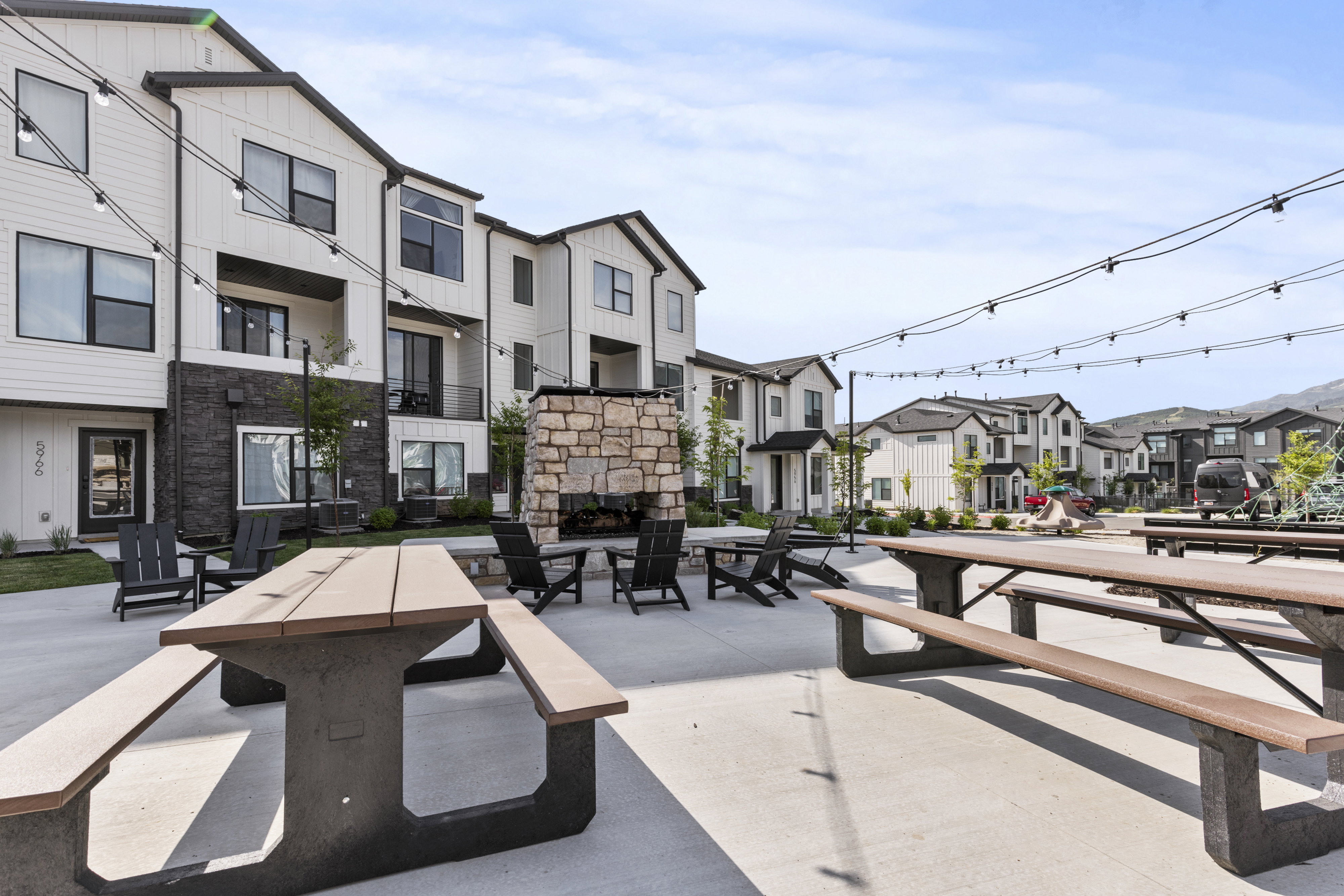 Outdoor patio featuring a stone fireplace, string lighting, and multiple picnic tables with benches