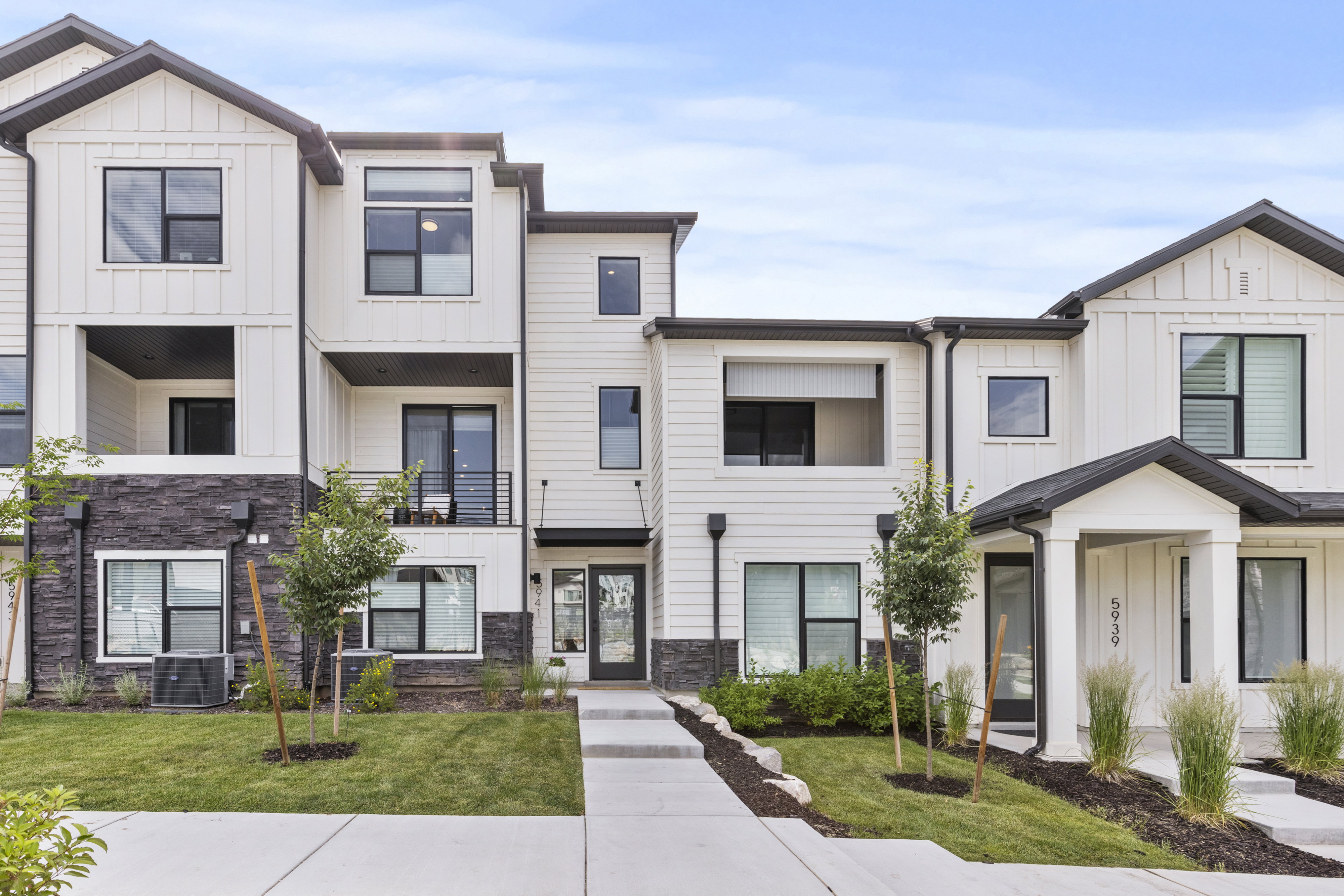 Modern townhome exterior featuring vertical and horizontal siding accents, dark stone veneer detailing, and black-framed windows