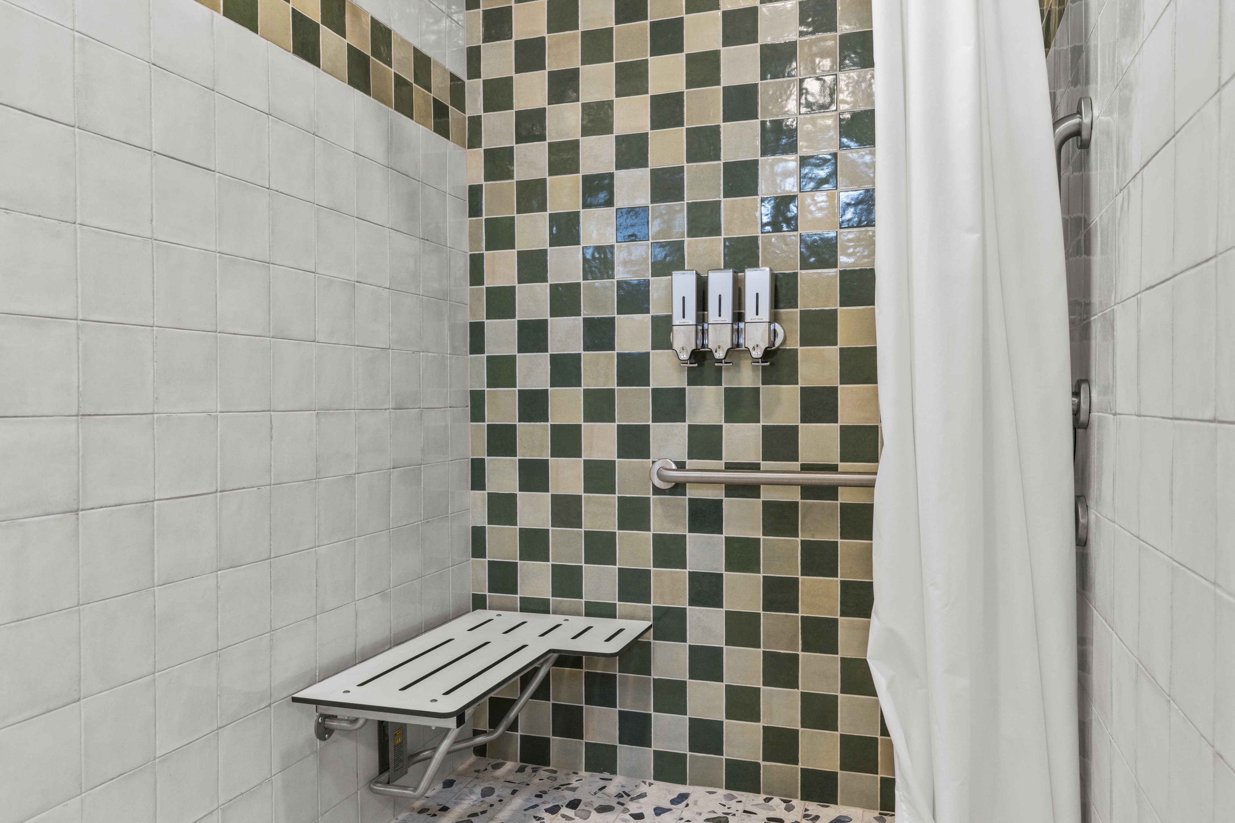 Shower enclosure featuring white and green checkerboard wall tiling, a built-in folding bench, and a coordinating green and white tiled border