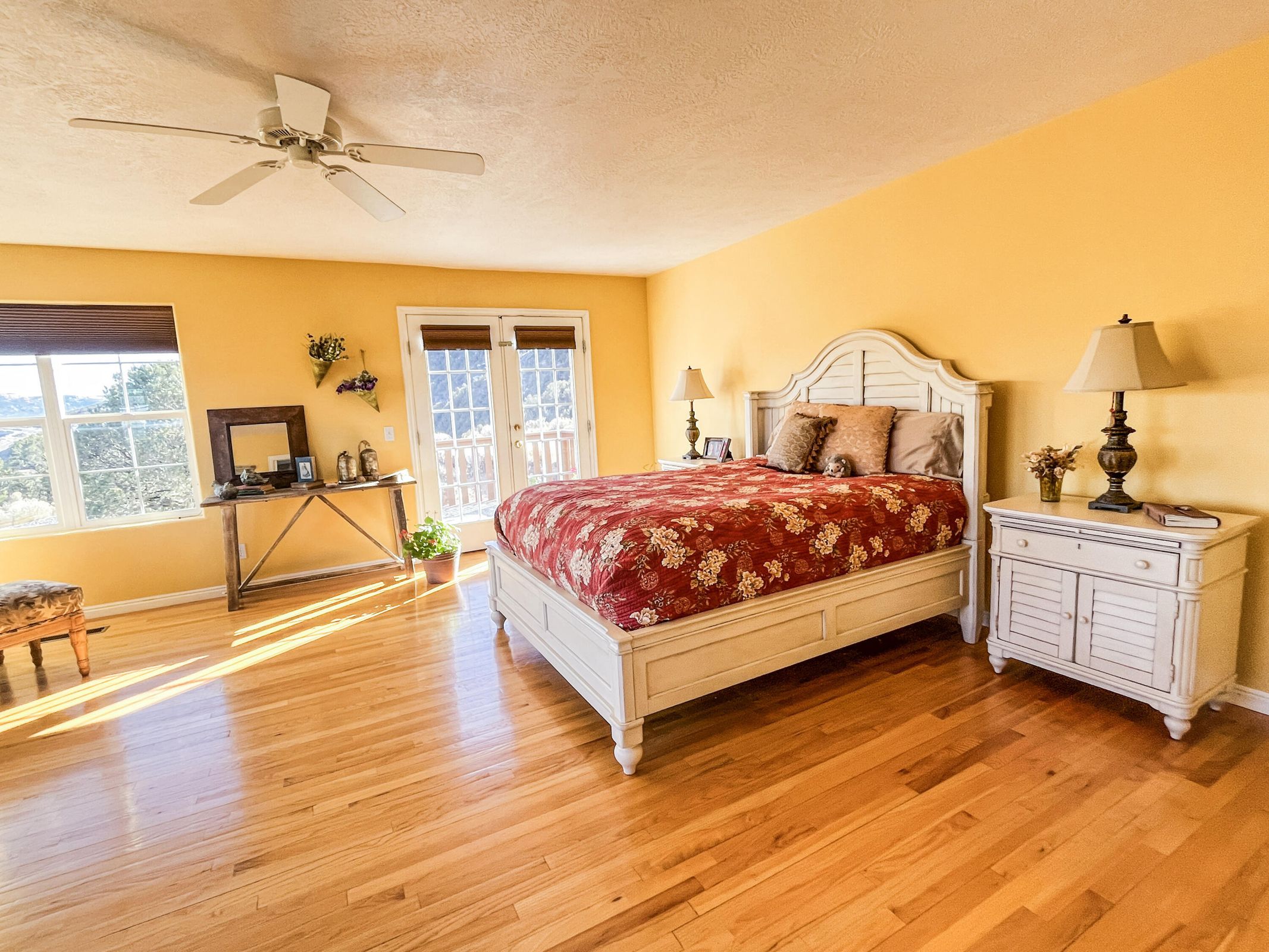 Hardwood flooring throughout featuring a ceiling fan, dual windows with blinds, and French doors