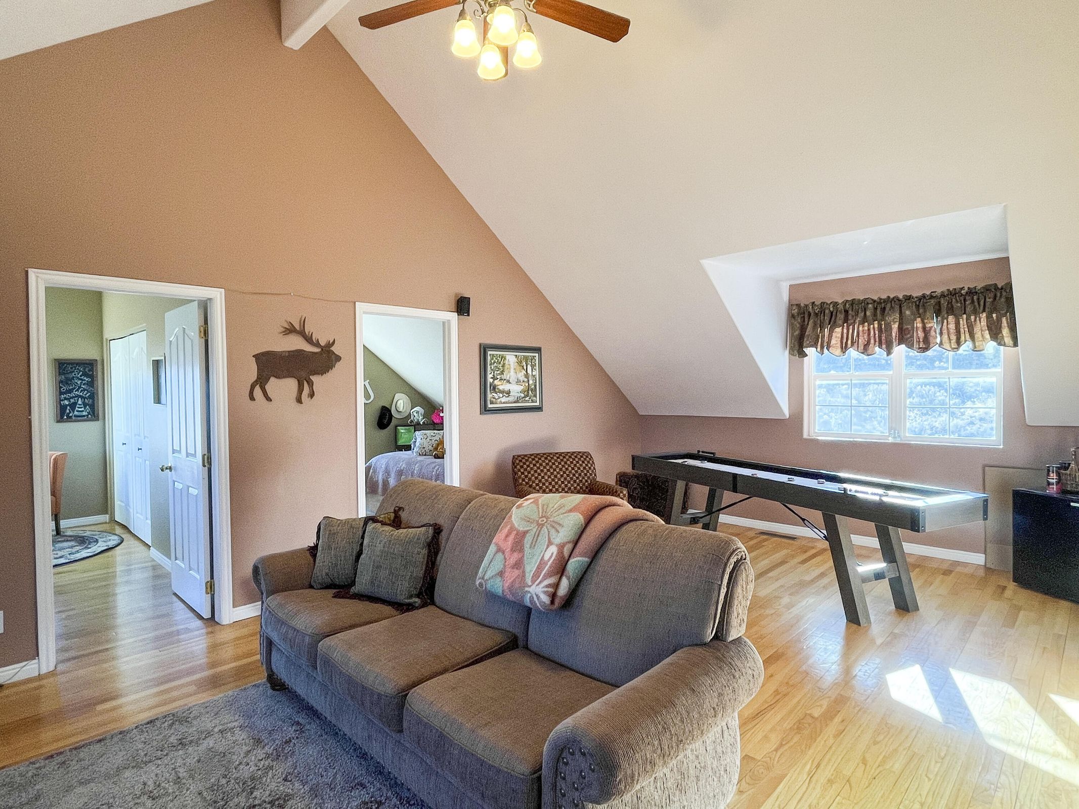 Vaulted ceilings with exposed beams and a ceiling fan enhance this space featuring wood-finish flooring