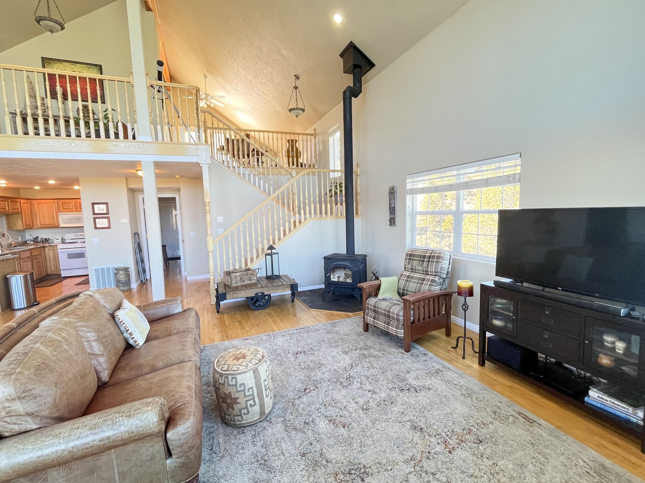 Vaulted ceiling great room featuring a wood-burning stove with a tall black flue, hardwood-finish flooring, and a multi-level staircase with wood railings