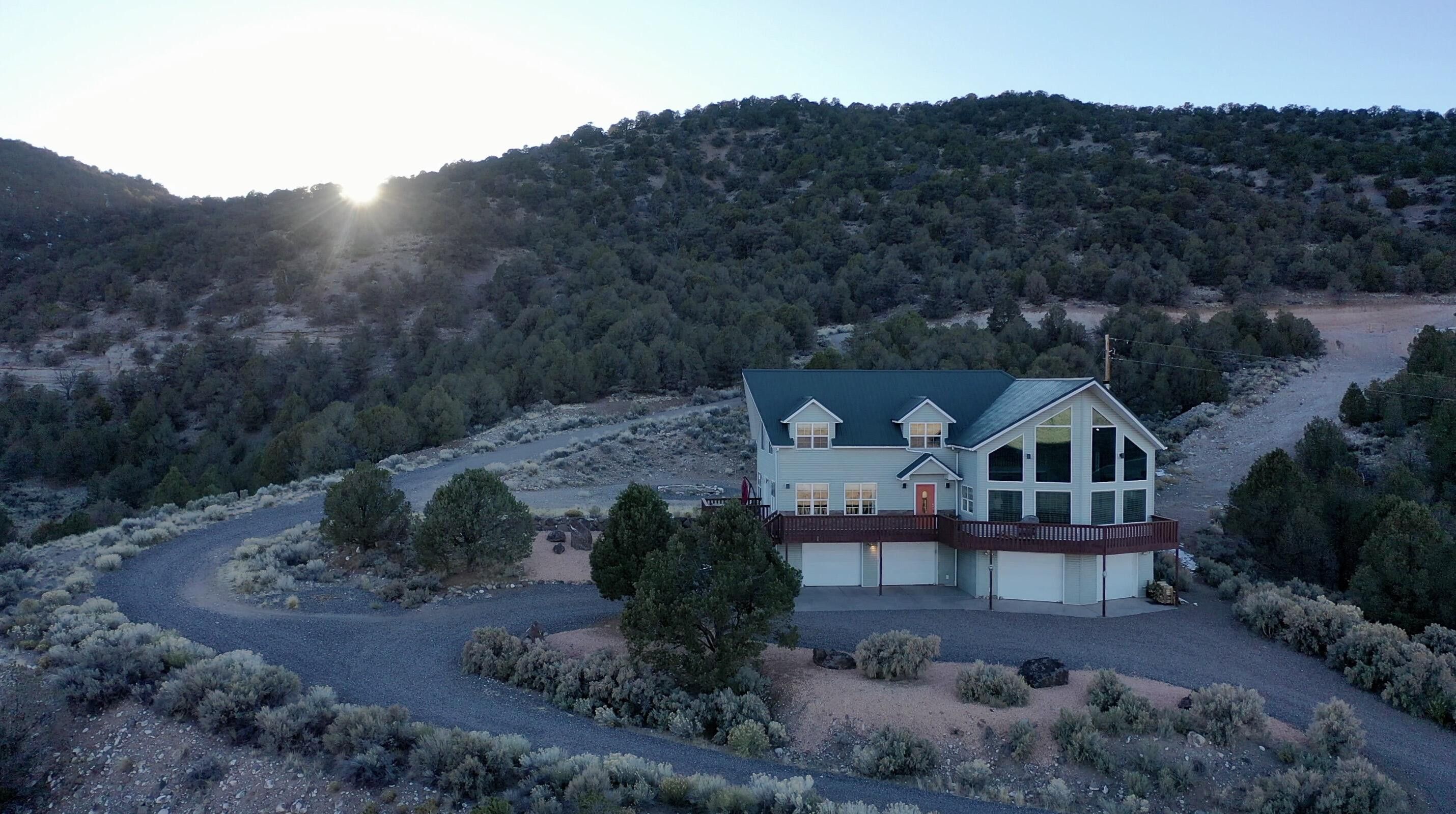 Hillside residence featuring multiple garage bays, a wrap-around deck, and abundant natural landscaping
