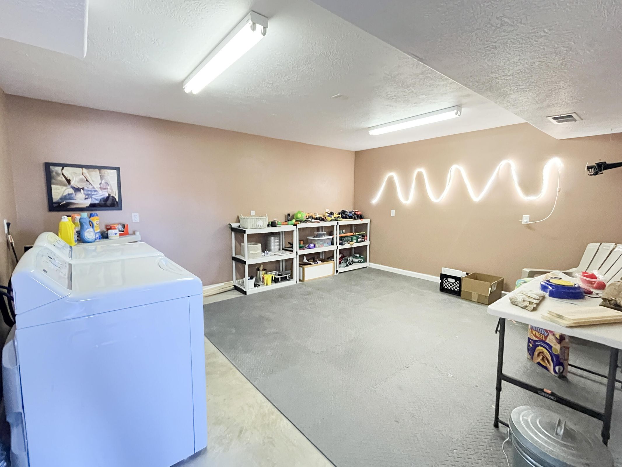 Spacious utility area featuring a concrete floor with partial rubber matting, fluorescent ceiling lights, and painted walls