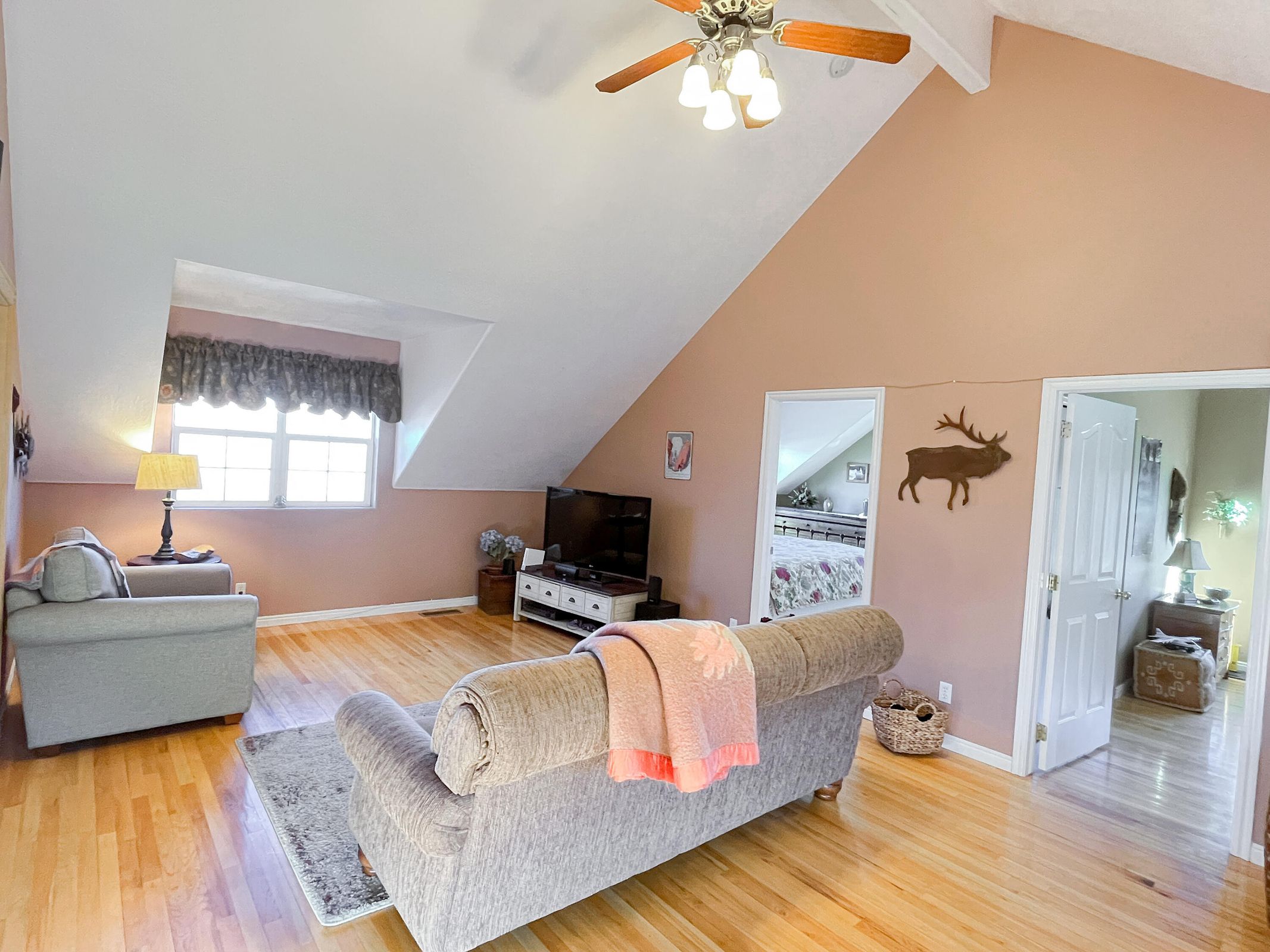 Spacious room with a vaulted ceiling, wood-finish flooring, ceiling fan, and multiple windows
