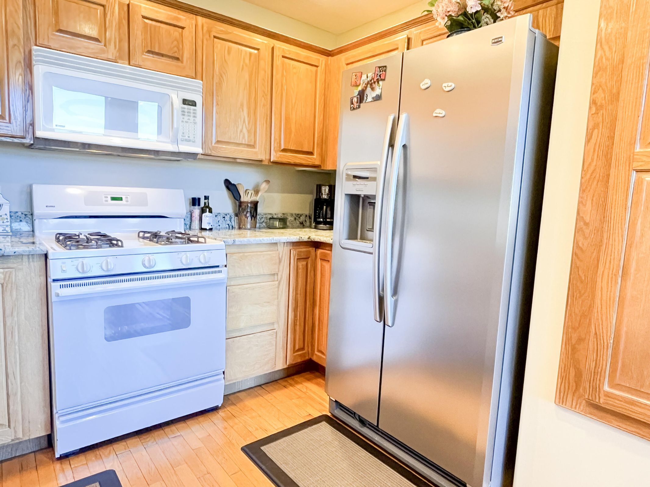 Kitchen featuring hardwood flooring, light wood cabinetry, white gas range with overhead microwave, stainless steel side-by-side refrigerator, and stone-look countertops