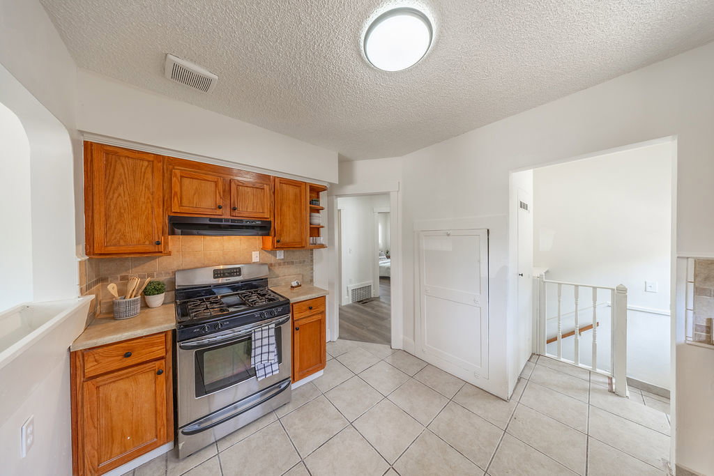 Kitchen featuring wood cabinetry, stainless steel range with overhead ventilation, stone-look countertops, and a tiled backsplash