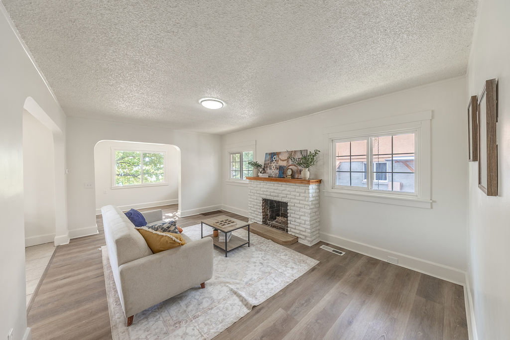 Living area featuring wood-finish flooring, a white brick fireplace with a wood mantle, and bright window lighting