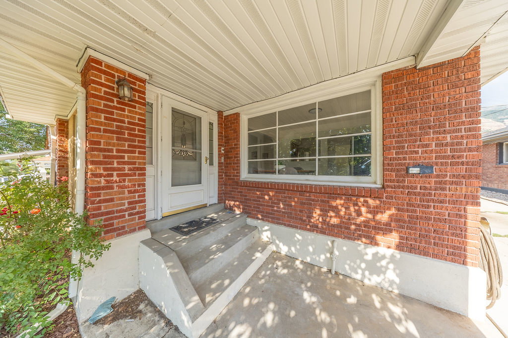 Brick exterior featuring a covered porch, concrete steps, and a white screen door