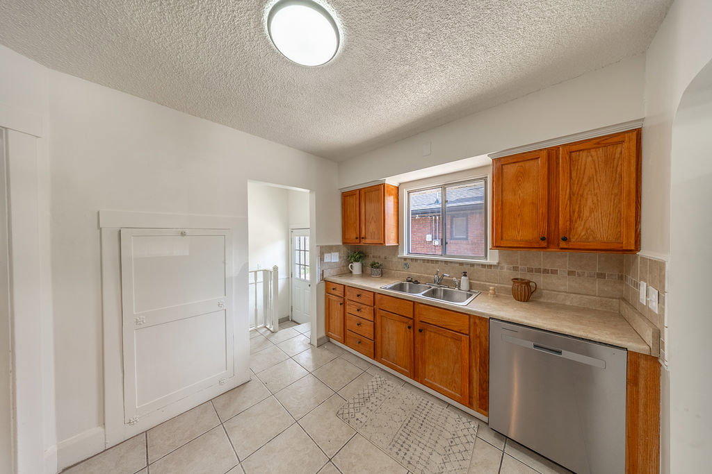 Kitchen featuring warm wood cabinetry, neutral countertops, a tile backsplash, and stainless steel dishwasher