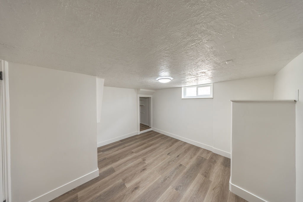 Spacious room featuring wood-finish flooring, white walls, and a visible window