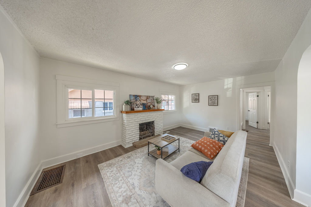 Living area featuring wood-finish flooring, white painted walls, and a white brick fireplace with a wood mantel