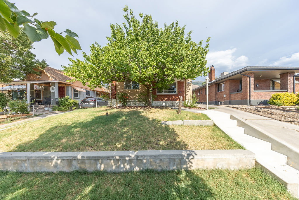 Front exterior with mature tree, sloped lawn, and concrete retaining wall