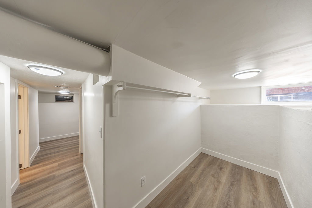Finished lower-level space featuring wood-finish flooring, recessed lighting, white walls, and a built-in hanging rod