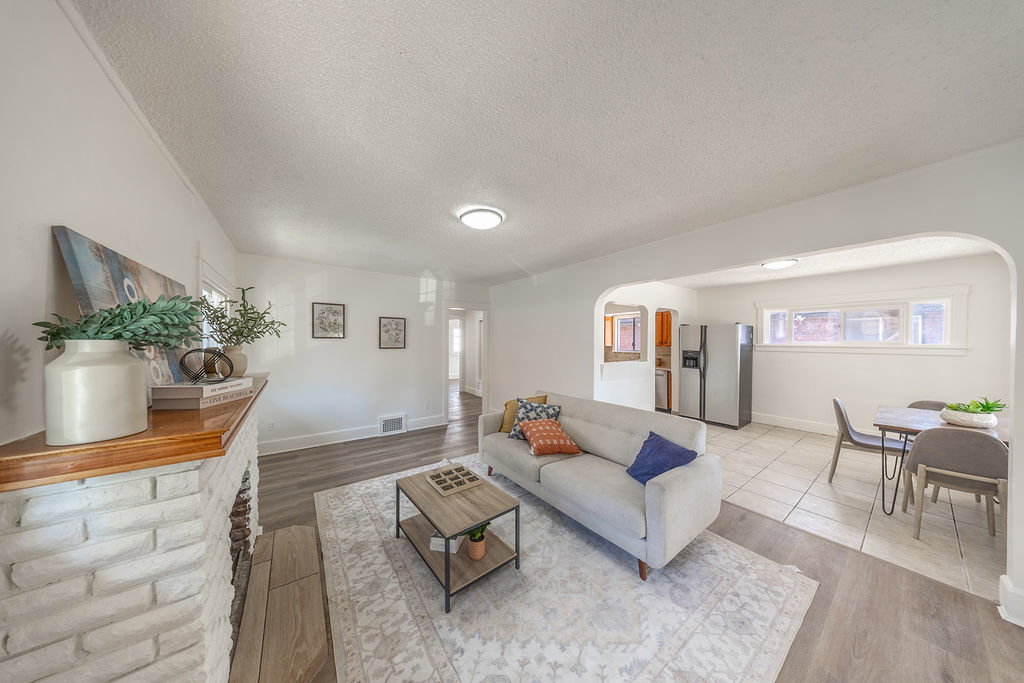Living area featuring a painted brick fireplace with a wood mantle, wood-finish flooring, and an arched entryway