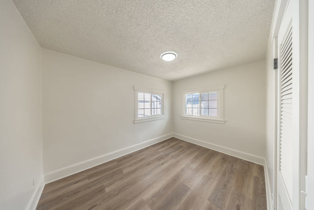 Room with wood-finish flooring, two window openings, and a louvered door