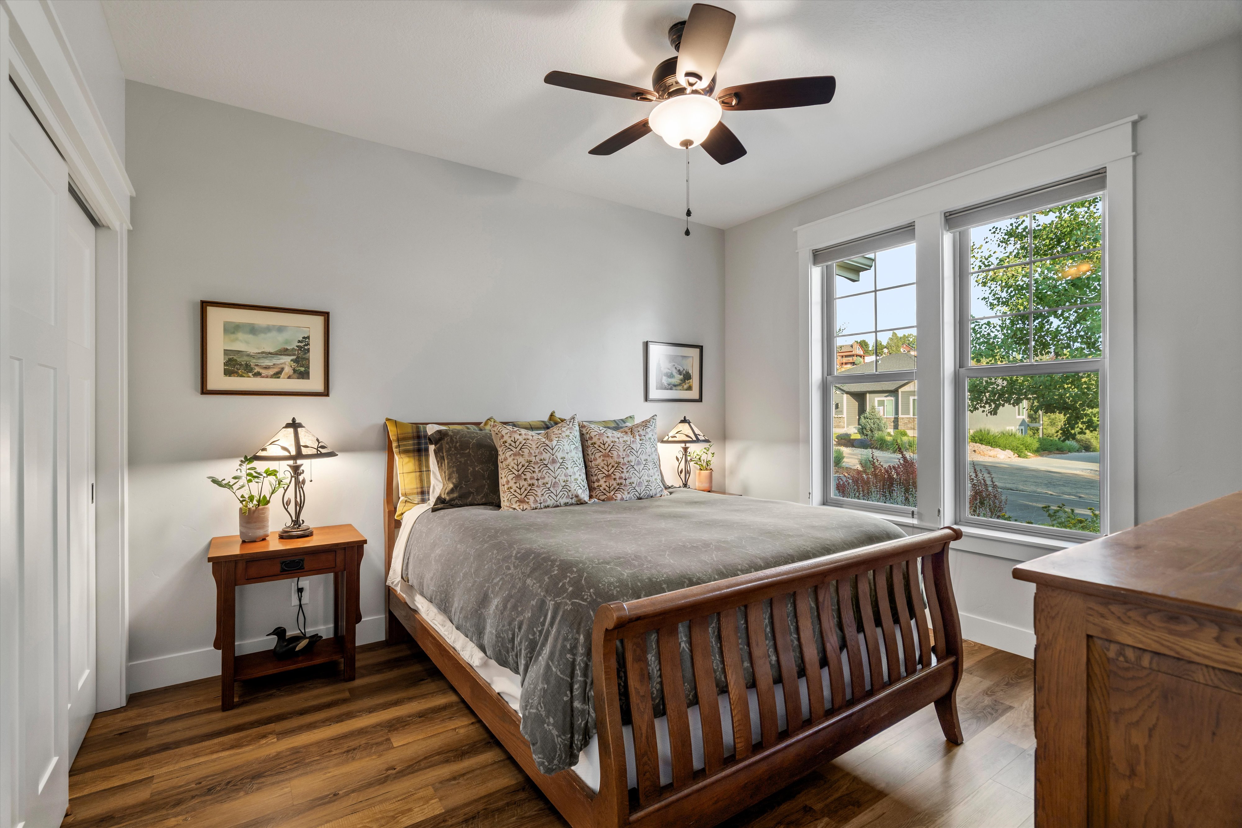 Room featuring wood-finish flooring, two window units, and a ceiling fan with integrated lighting