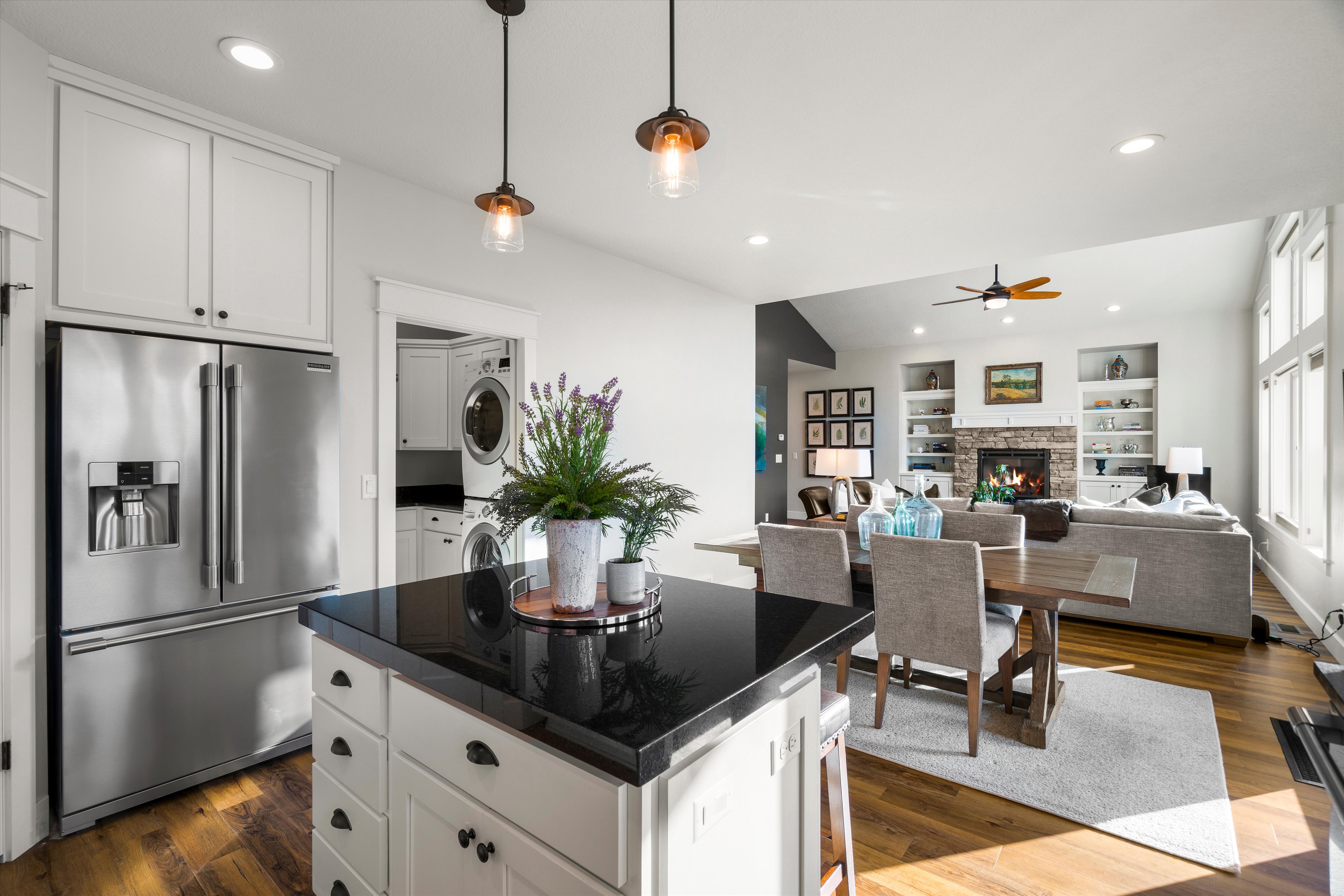 Open-concept living space featuring a kitchen island with dark stone countertop, stainless steel refrigerator, hardwood-finish flooring, a fireplace with stone surround, and built-in shelving