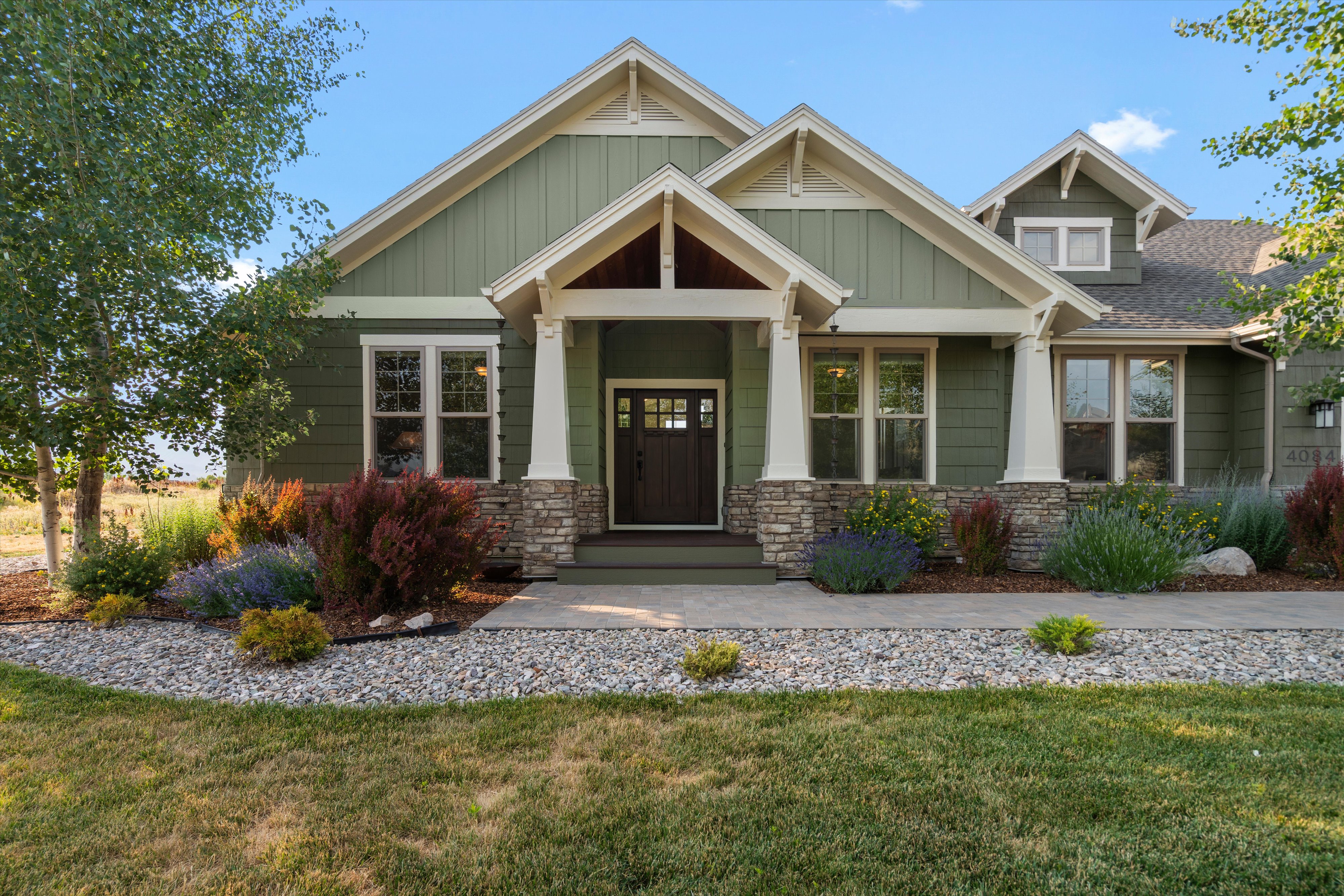 Craftsman-style exterior featuring a covered entry, stone column bases, green siding, and decorative gable accents