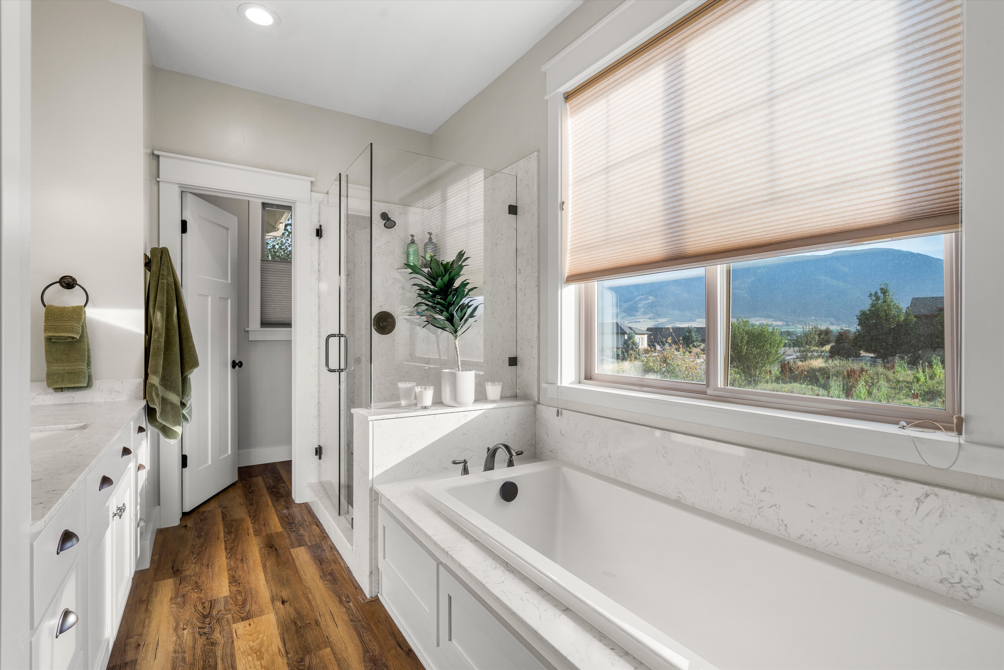 Freestanding bathtub with surrounding stone-finish decking, glass-enclosed shower, wood-finish flooring, and white vanity with stone-finish countertop