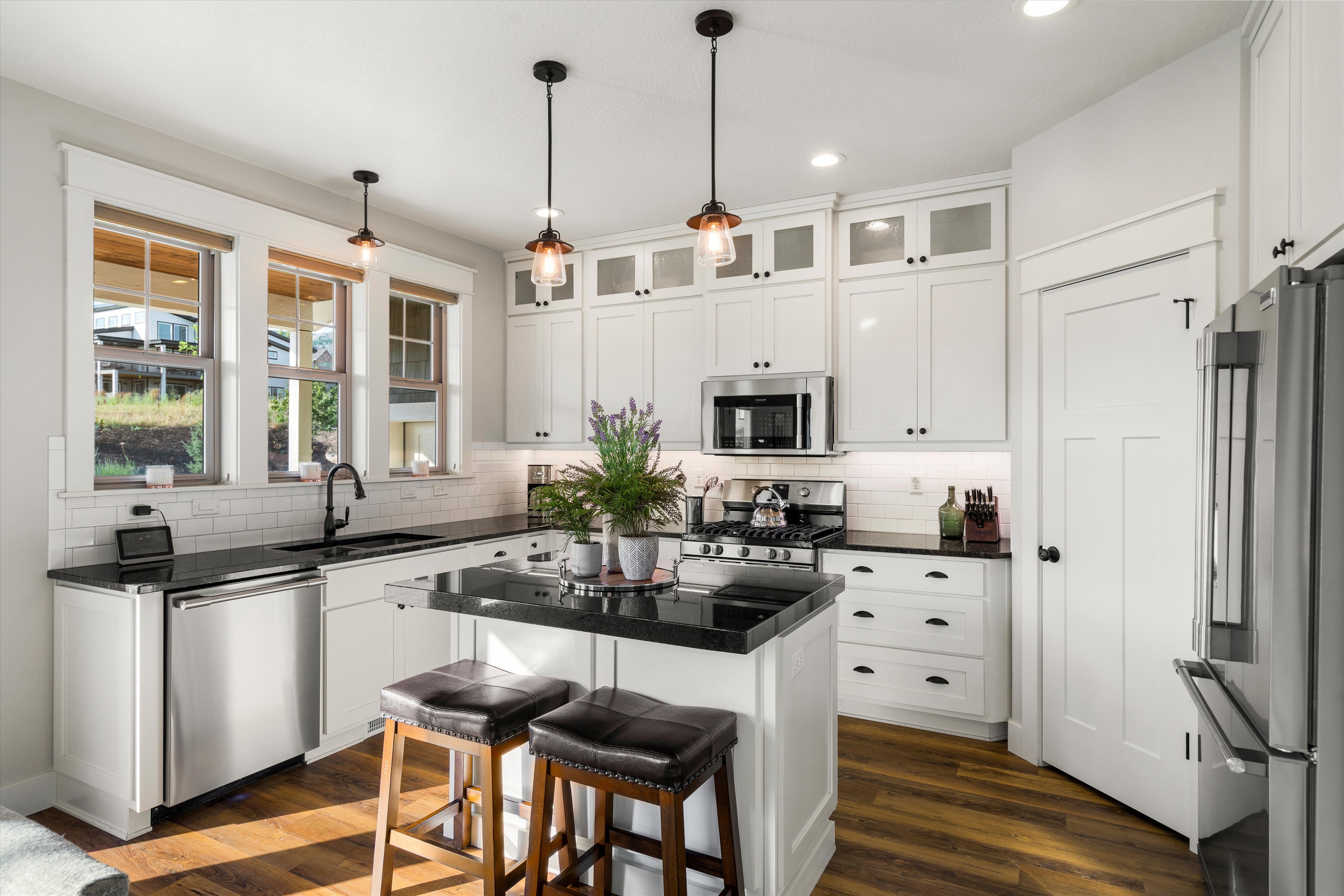 Modern kitchen featuring white shaker cabinetry with upper glass-front cabinets, stainless steel appliances, a center island with bar seating, and dark countertops