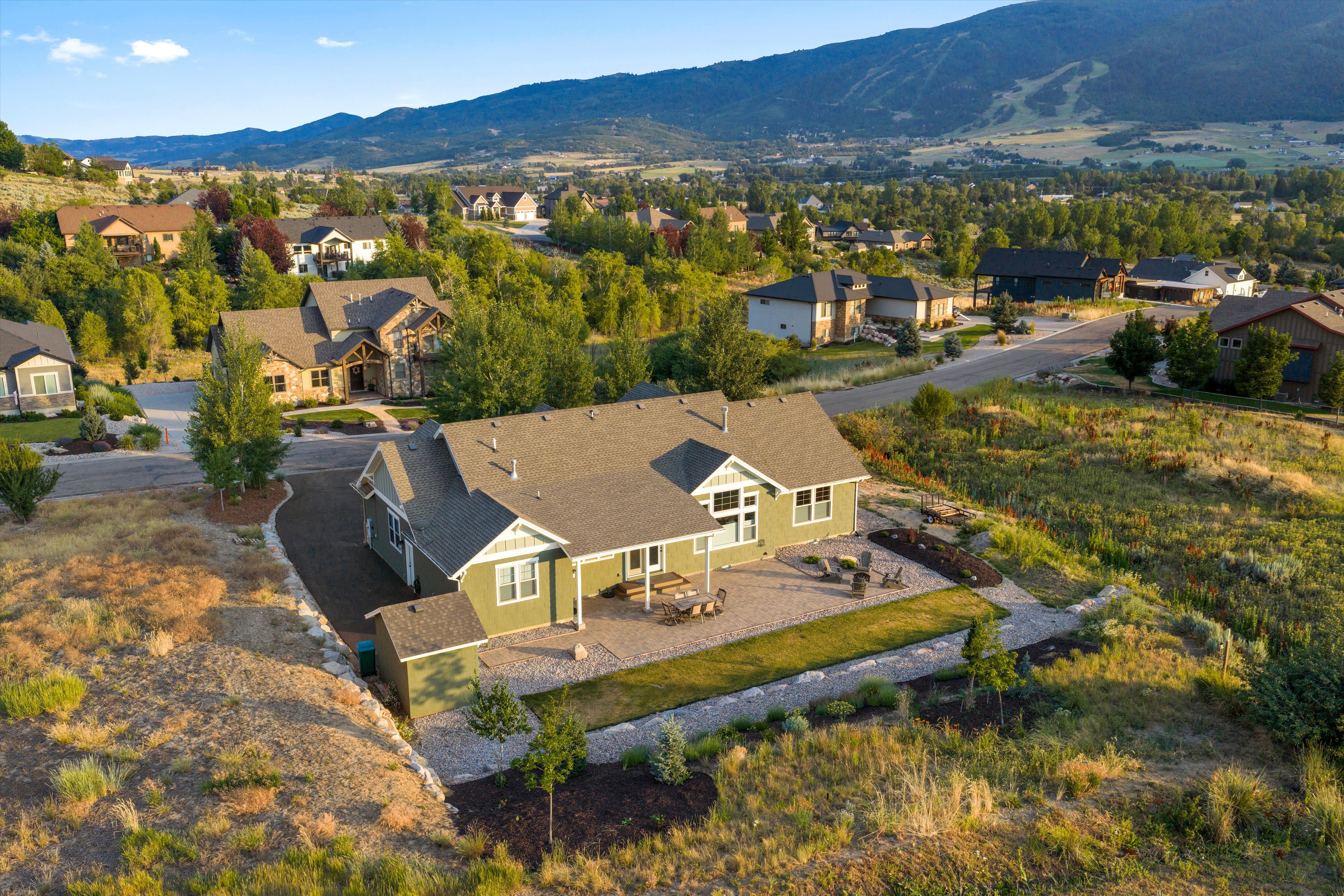 Single-story residence with a green exterior, a patio with pavers, a terraced landscape, and a surrounding natural environment