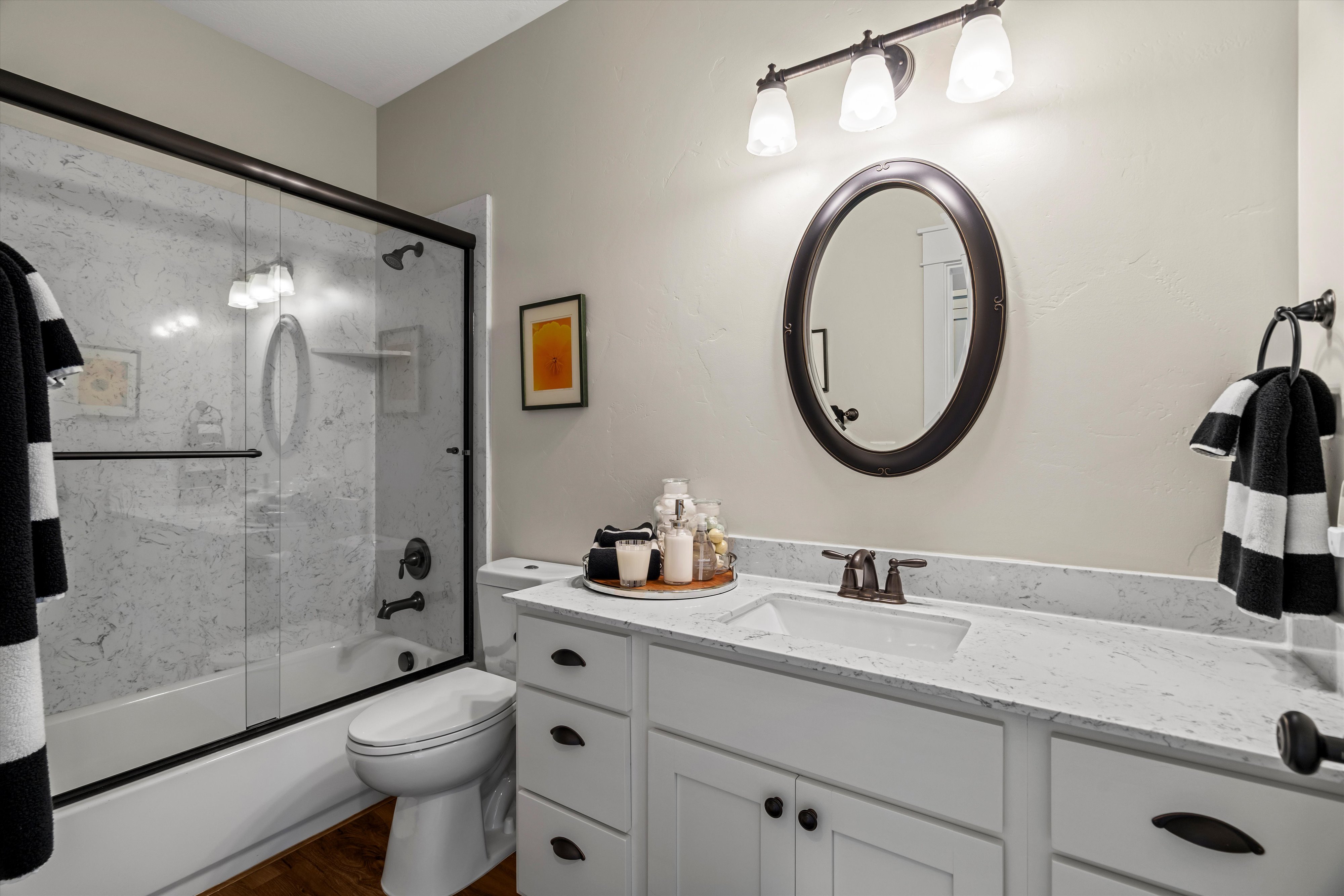 Bathroom featuring a white vanity with a white countertop, an oval mirror, and a shower-tub combination with a glass enclosure