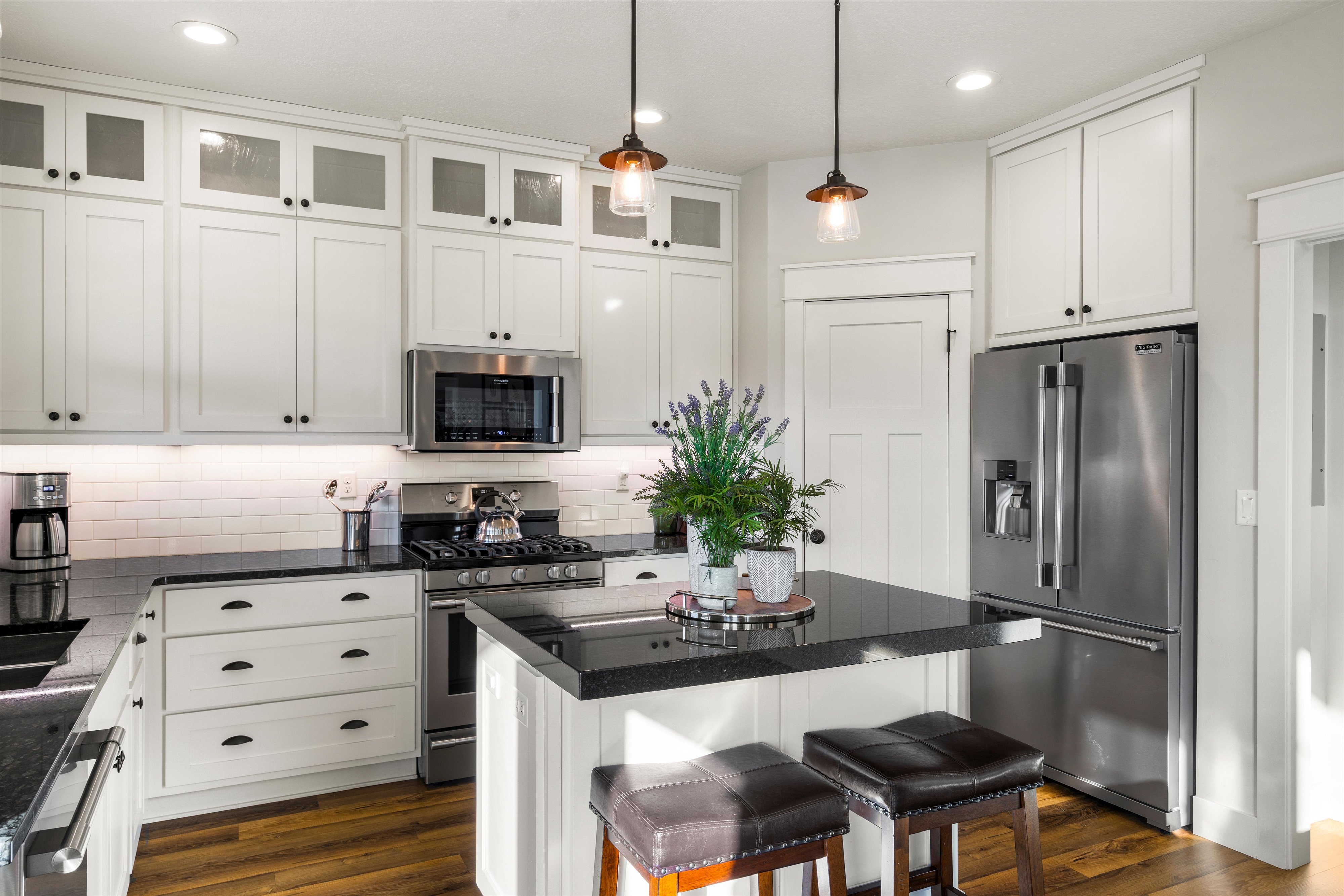 Kitchen featuring white shaker-style cabinetry, dark countertops, stainless steel appliances, and wood-finish flooring