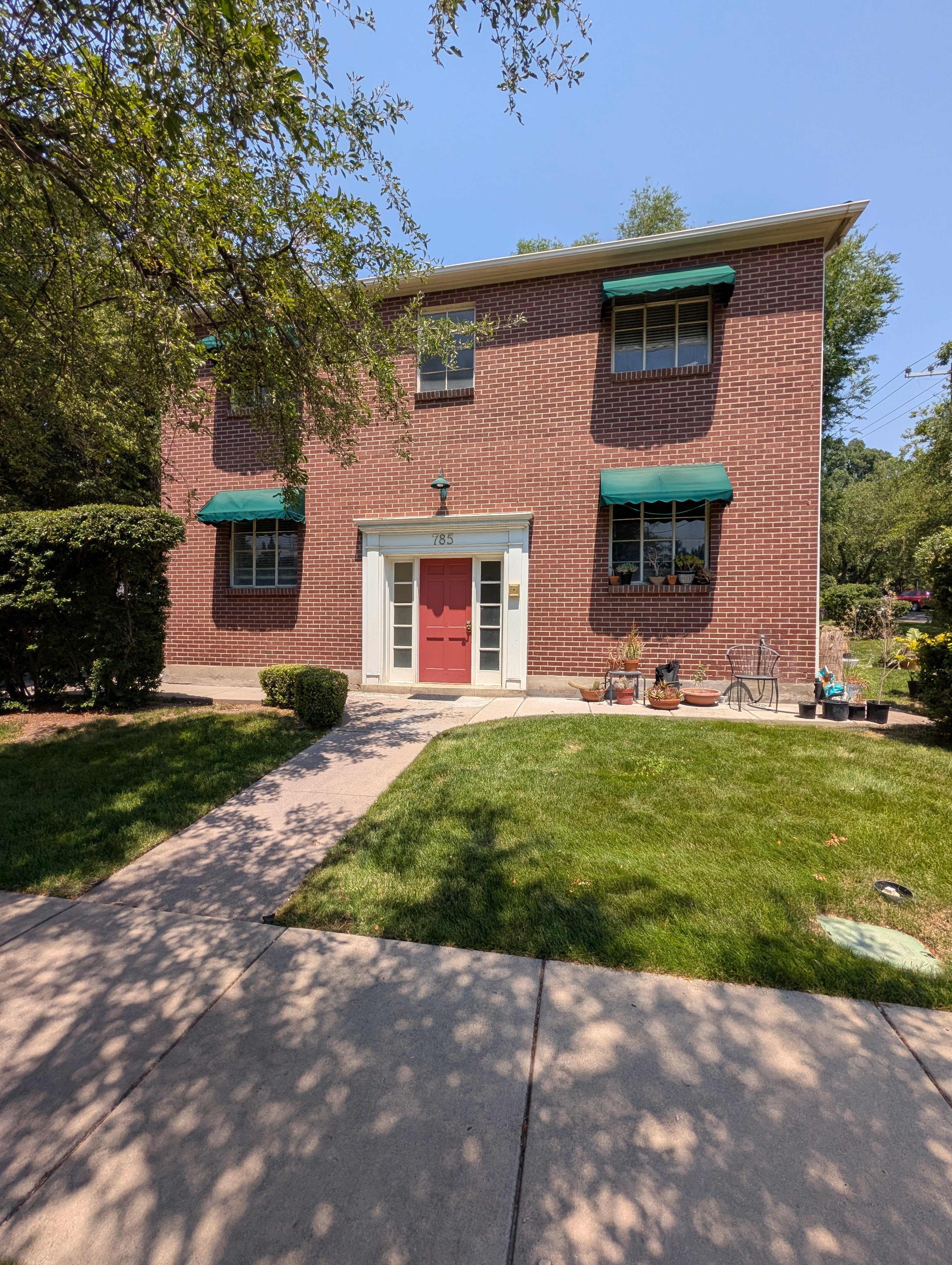 Brick facade residence featuring a red entry door, white door surround, and green window awnings