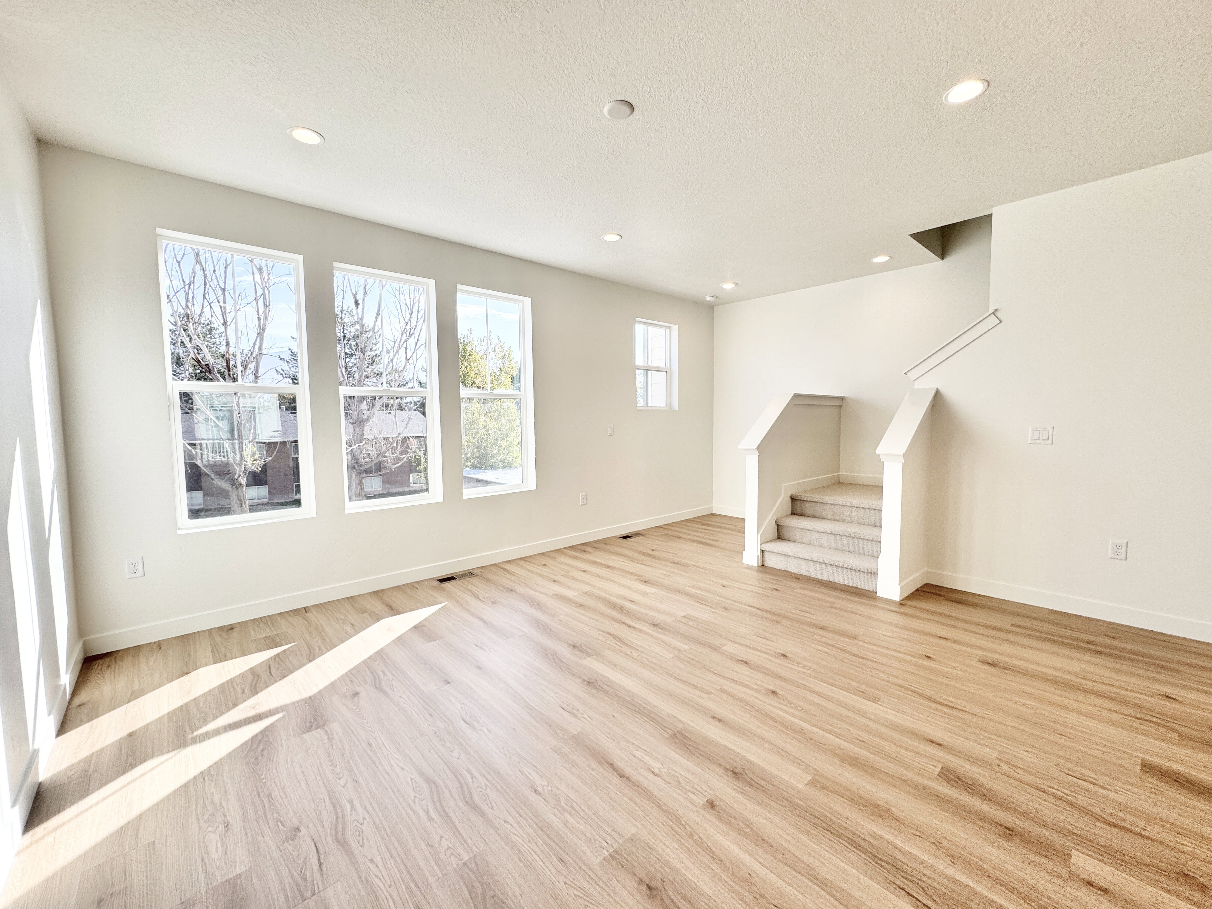 Spacious interior featuring wood-finish flooring, recessed lighting, and a staircase with carpeted treads